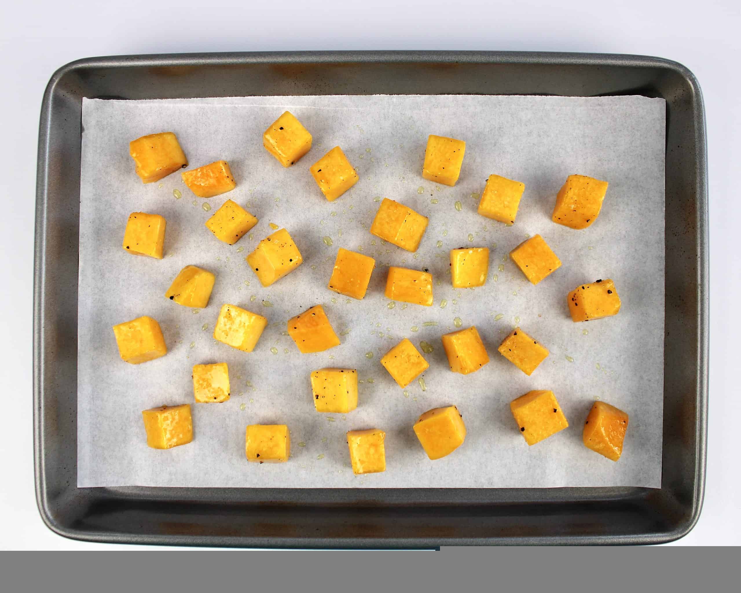 cubes of butternut squash with olive oil salt and pepper on parchment lined baking sheet
