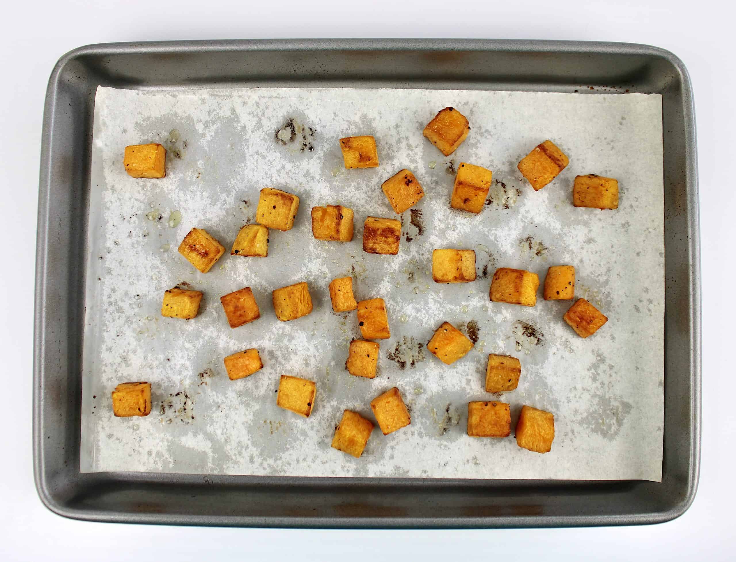 cubes of roasted butternut squash with olive oil salt and pepper on parchment lined baking sheet