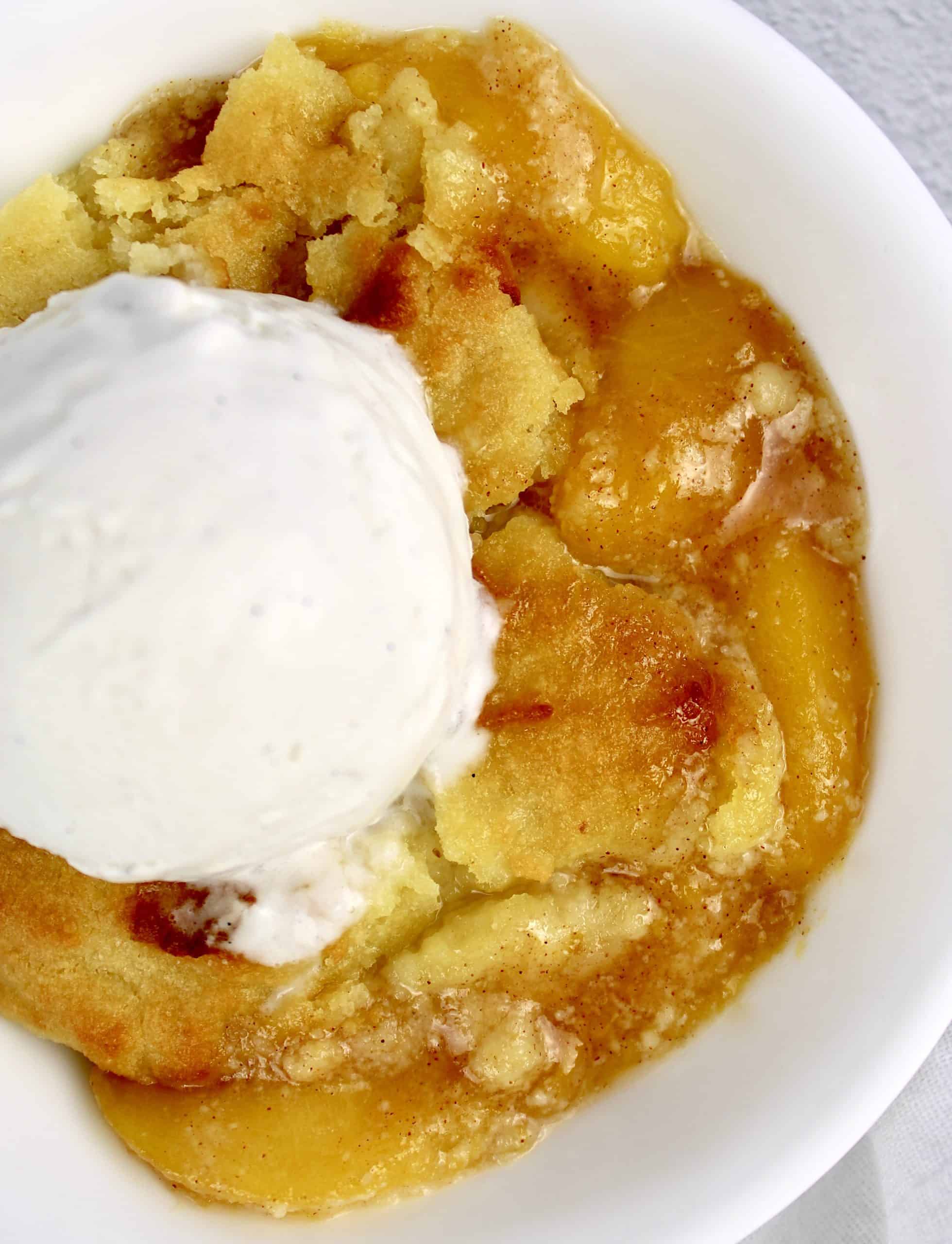 Peach Cobbler in white bowl with scoop of vanilla ice cream on top