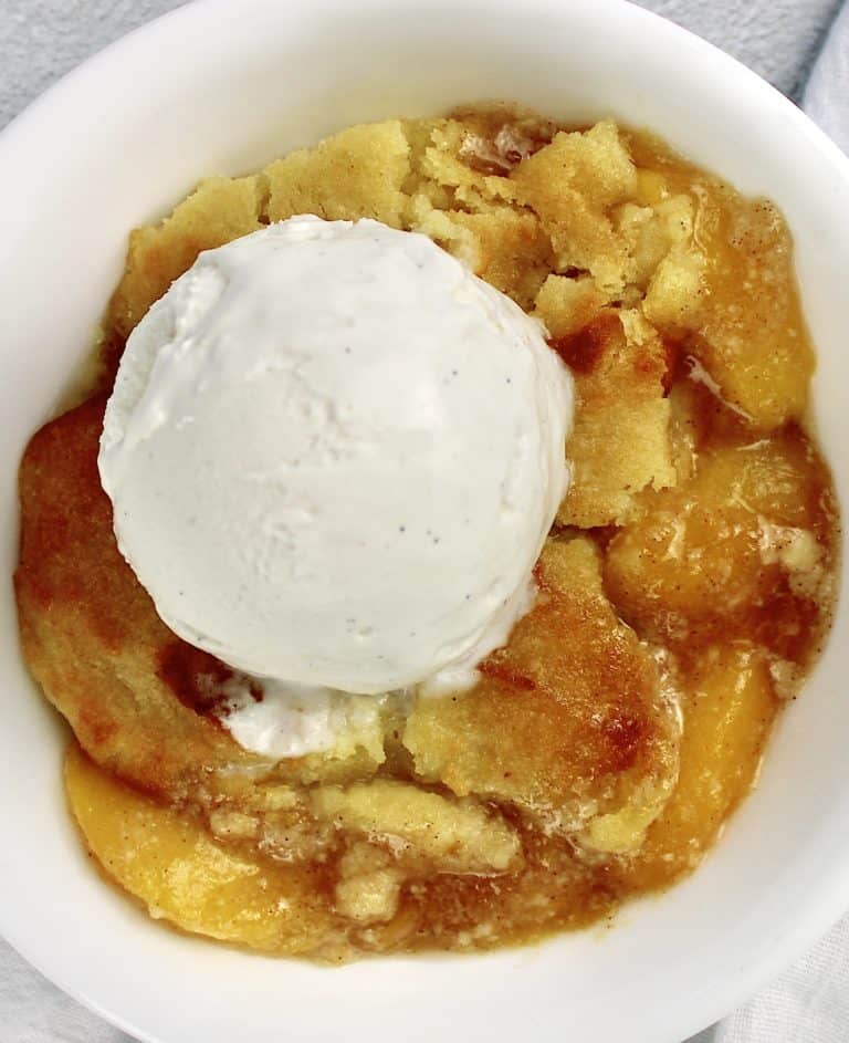 peach cobbler in white bowl with scoop of vanilla ice cream on top