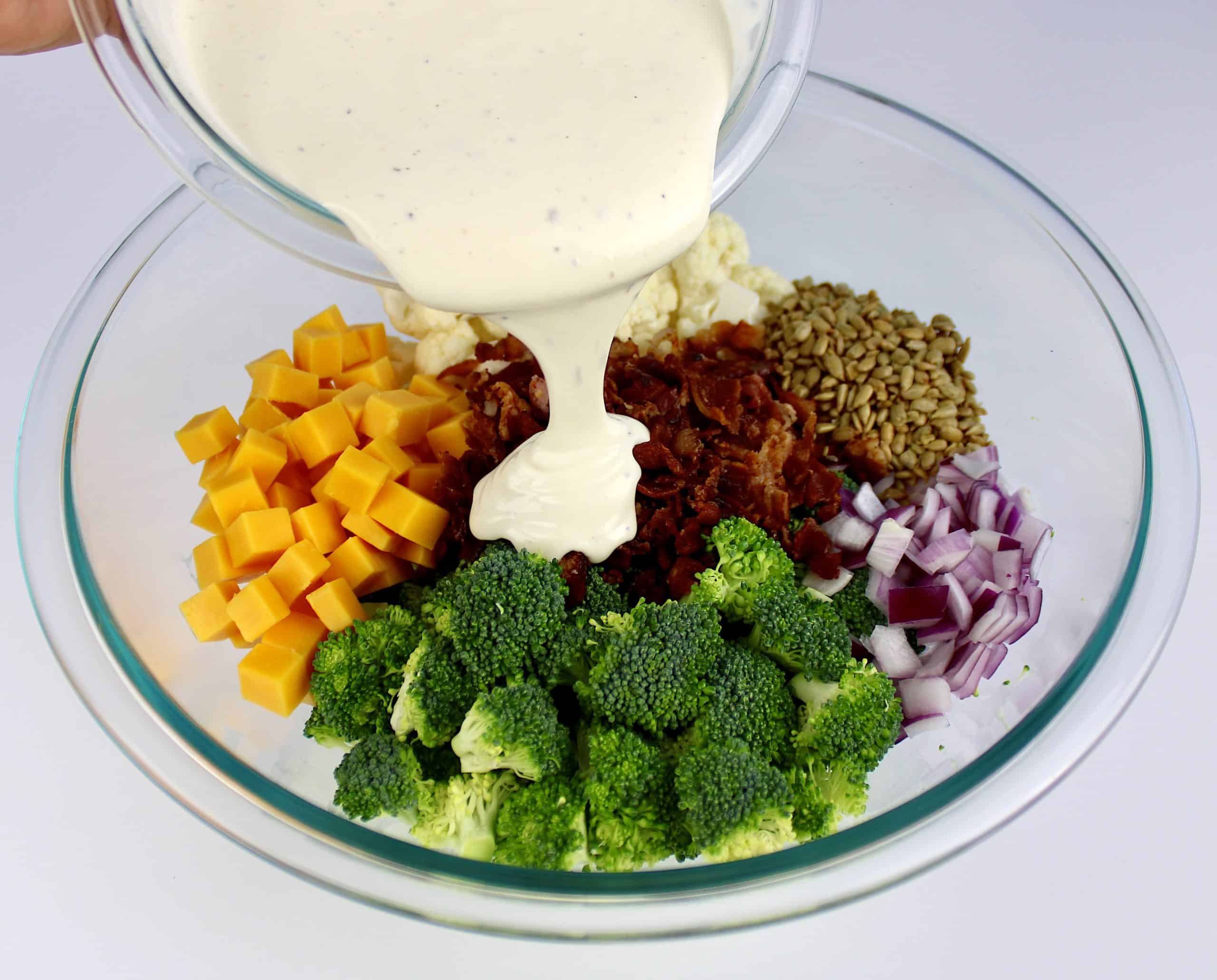 dressing being poured into bowl with Broccoli Cauliflower Salad ingredients