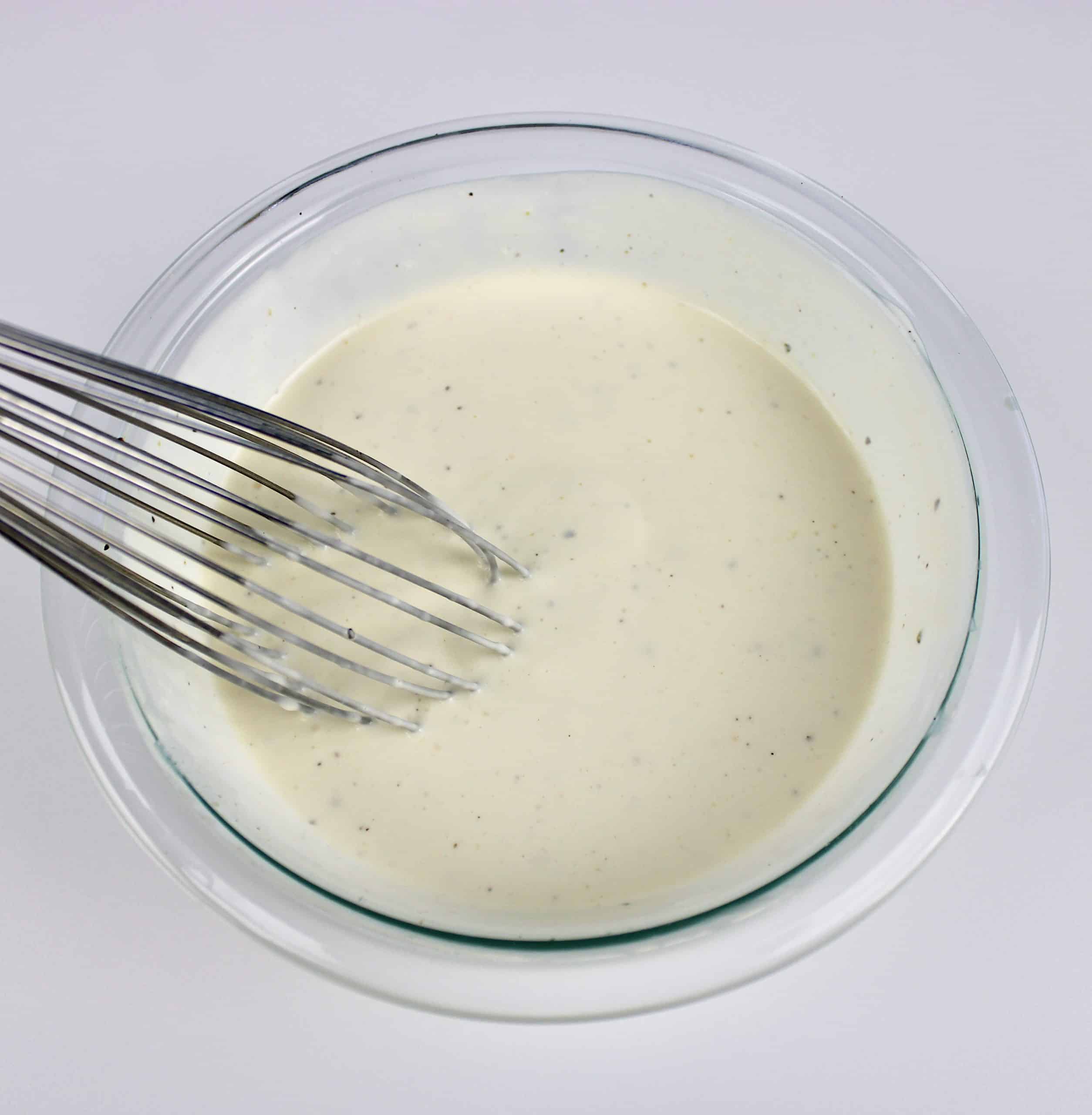 Broccoli Cauliflower Salad dressing in glass bowl with whisk