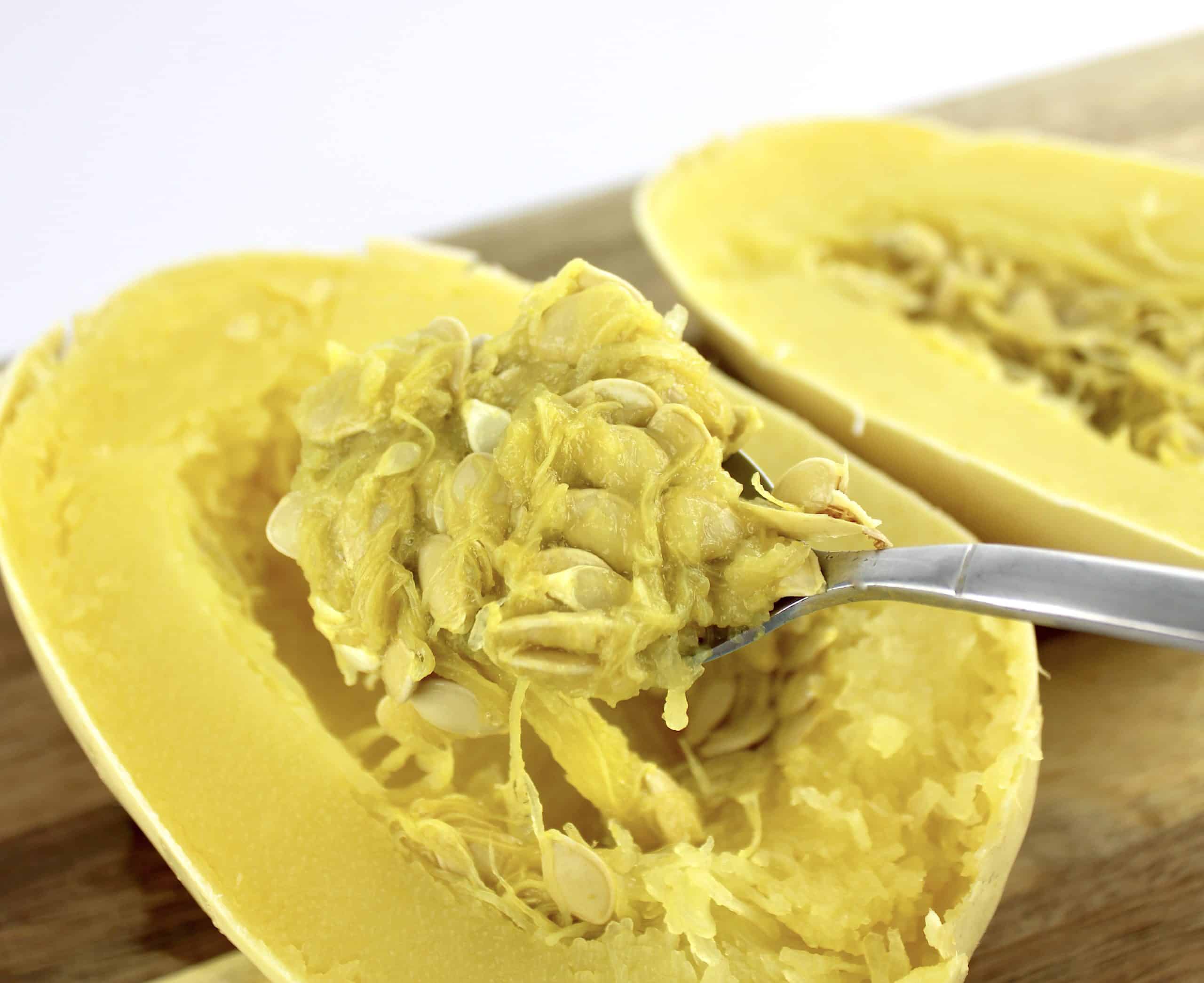seeds and pulp being scooped out of spaghetti squash cut in half