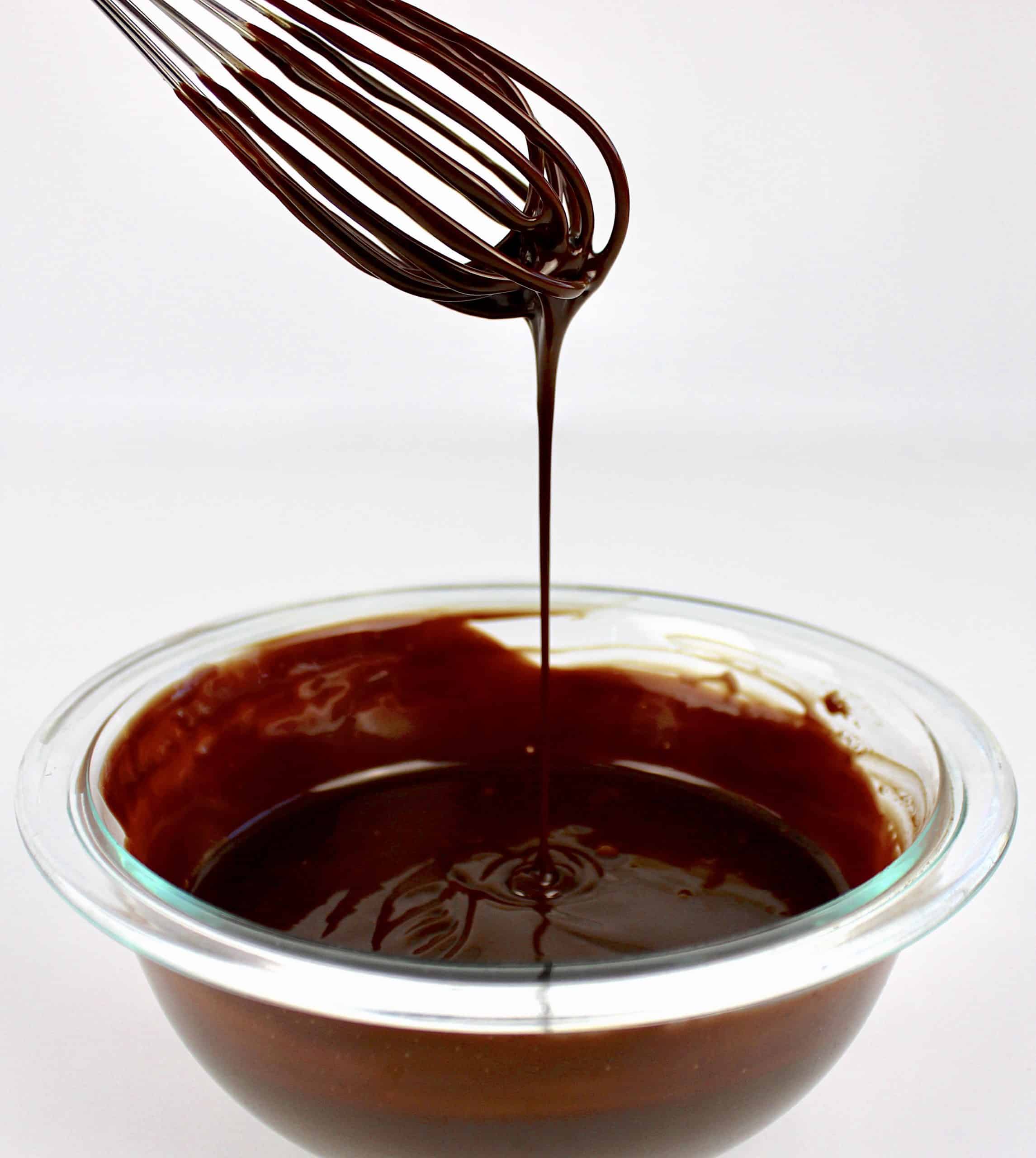 chocolate sauce in glass bowl being dripped from whisk