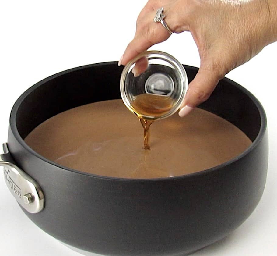 vanilla extract being poured into hot chocolate in saucepan