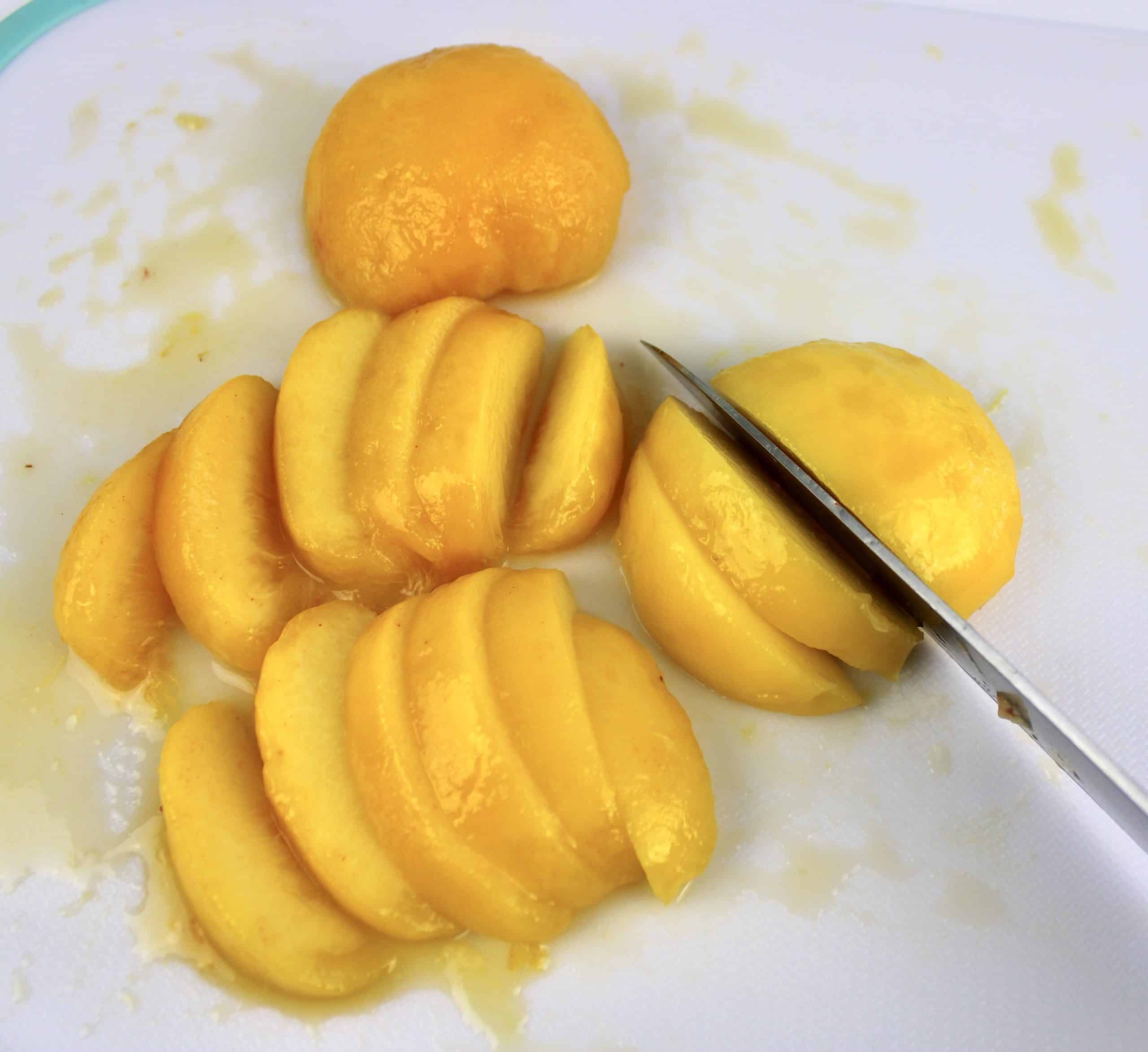 slices of fresh peaches and knife on white cutting board