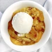peach cobbler in white bowl with scoop of vanilla ice cream on top