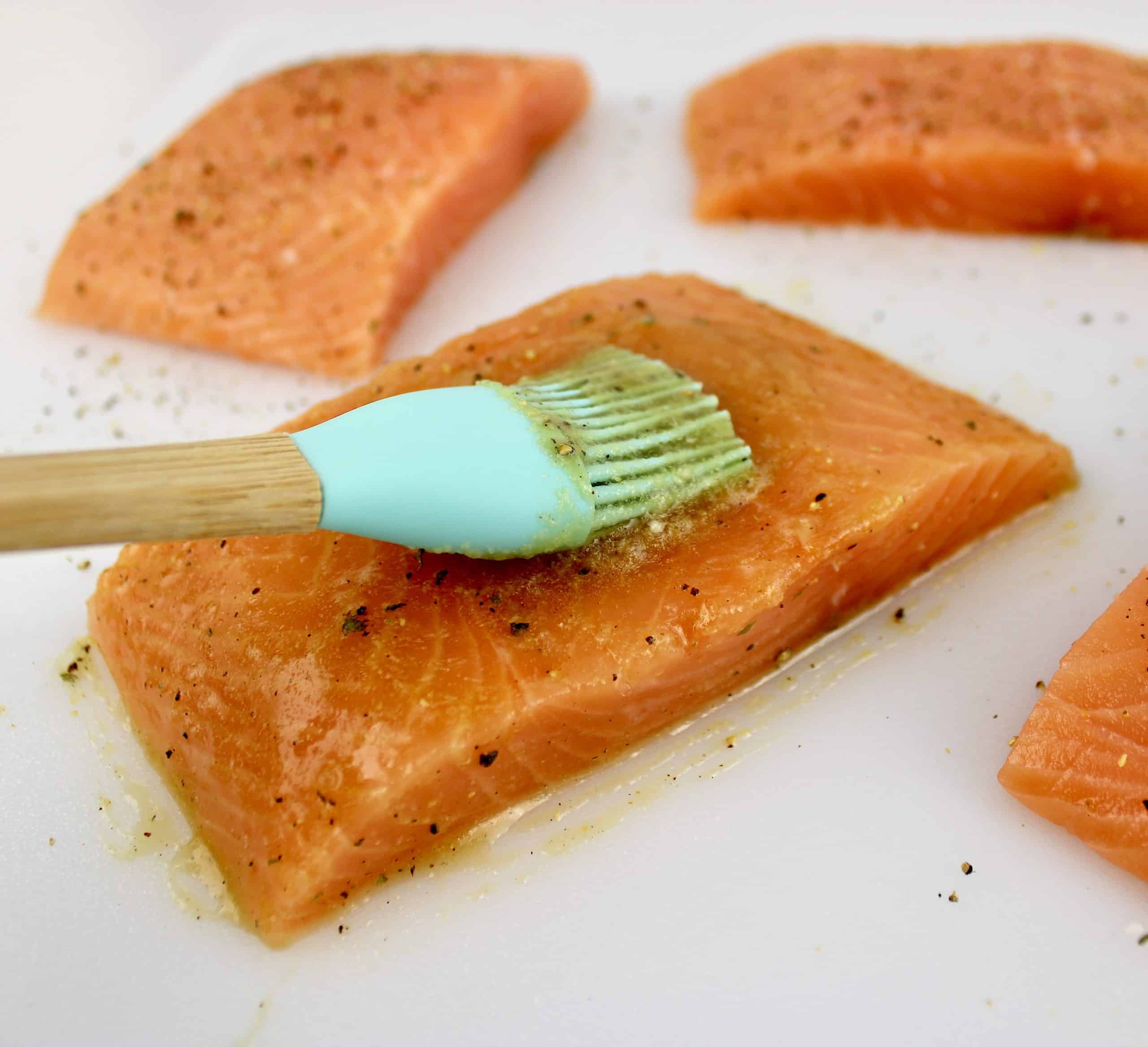 maple syrup mixture being brushed over salmon on white cutting board