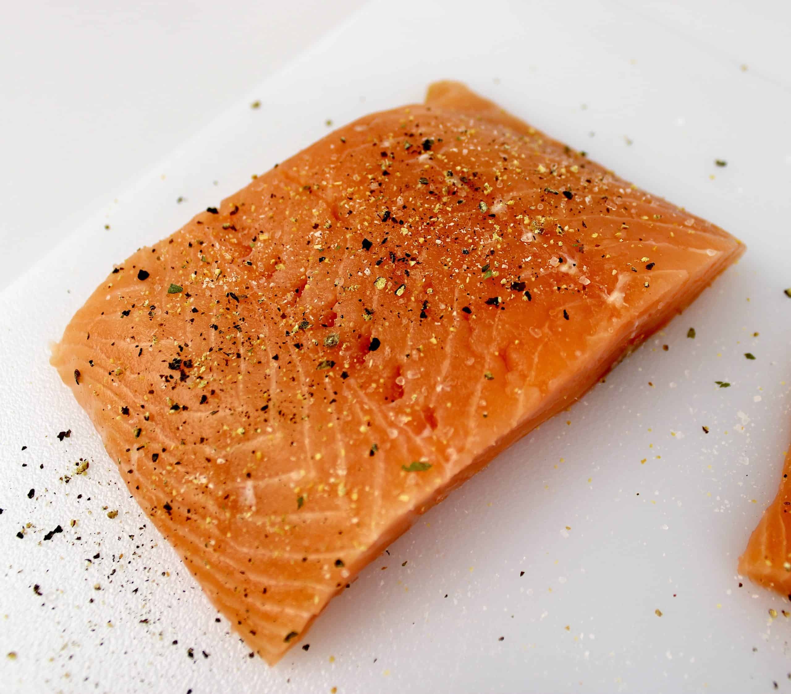 piece of salmon on white cutting board with salt and pepper