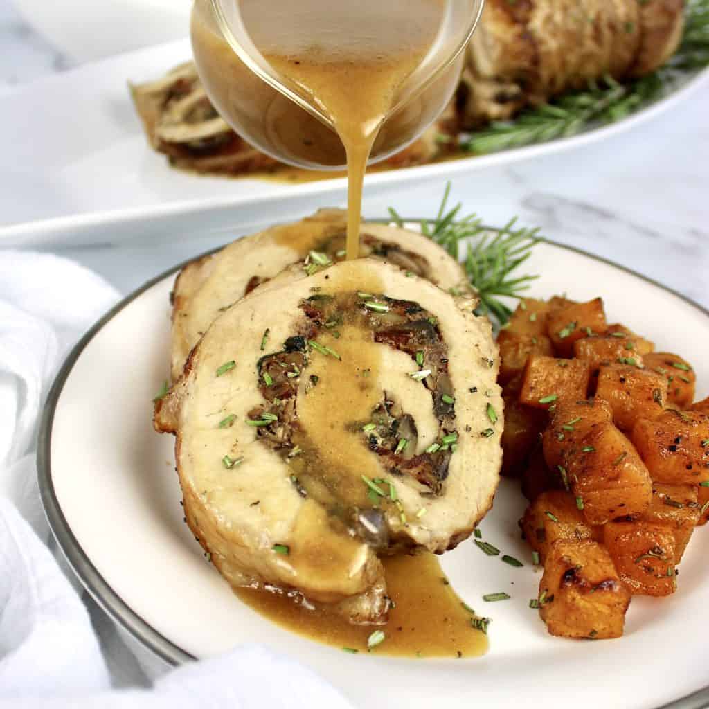 Stuffed Pork Loin with gravy being poured over top and butternut squash on side