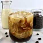 Cold Brew Coffee in glass with creamer and coffee beans in background