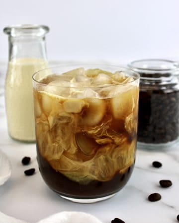 Cold Brew Coffee in glass with creamer and coffee beans in background