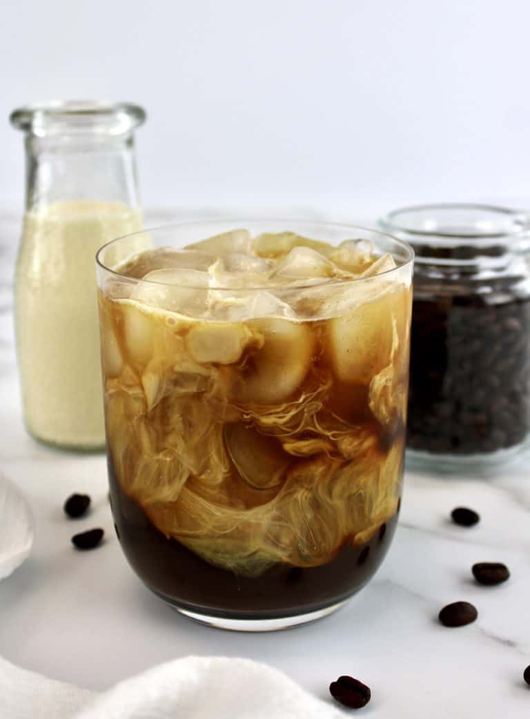 Cold Brew Coffee in glass with creamer and coffee beans in background