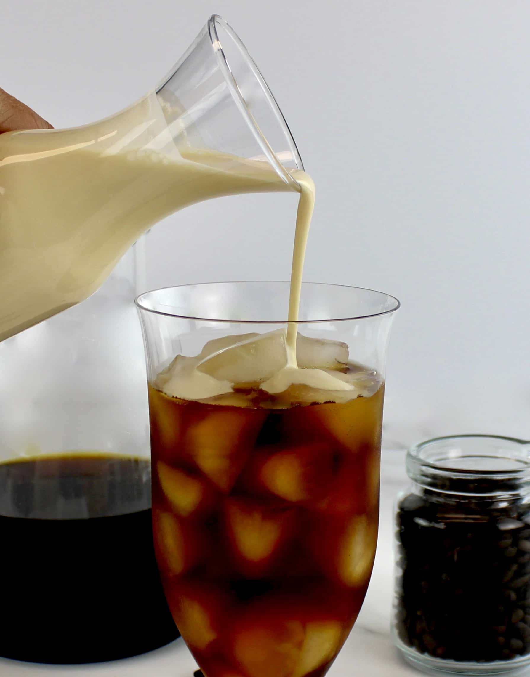 creamer being poured over iced coffee in glass