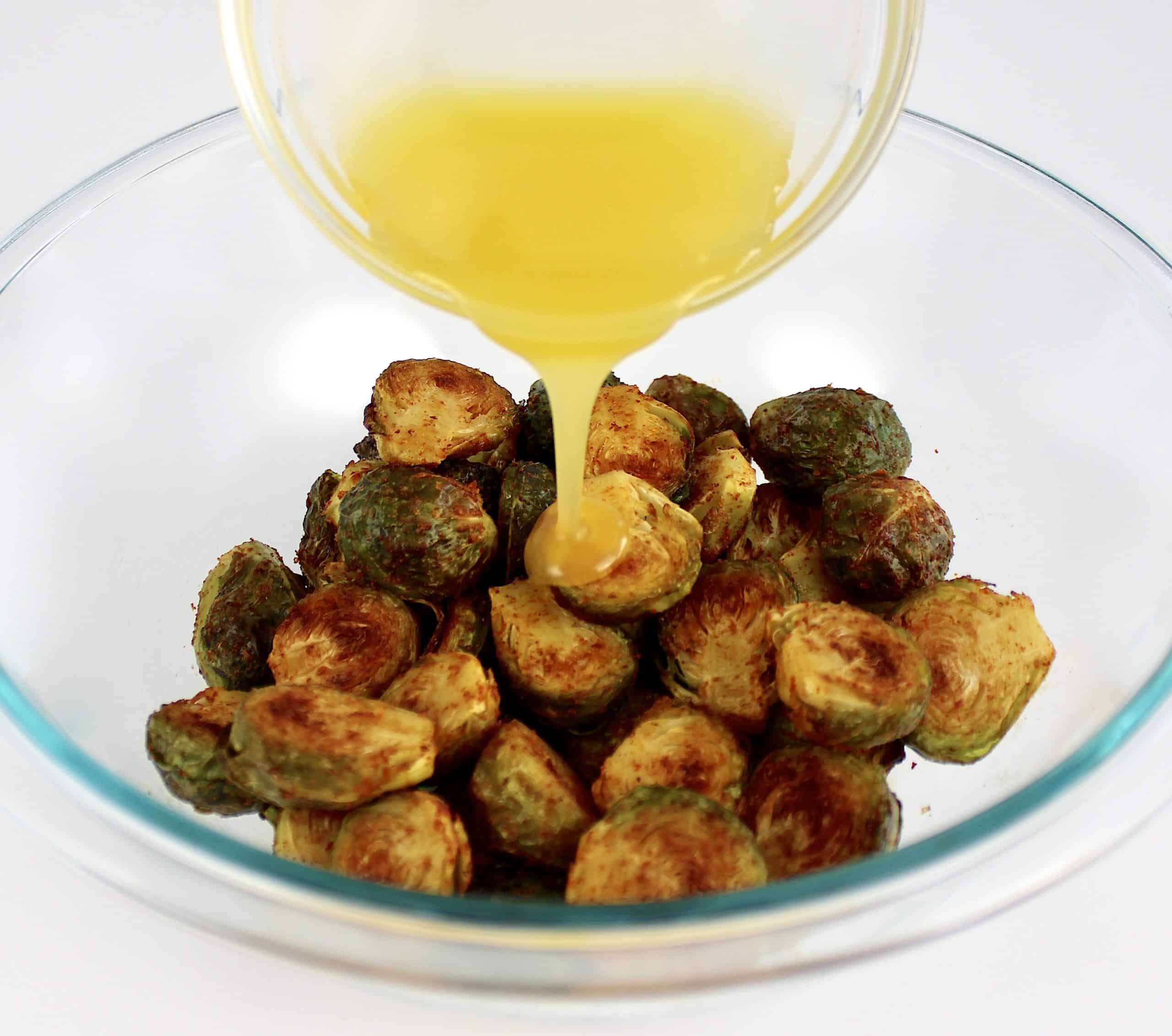 honey butter being poured over roasted brussels sprouts in glass bowl