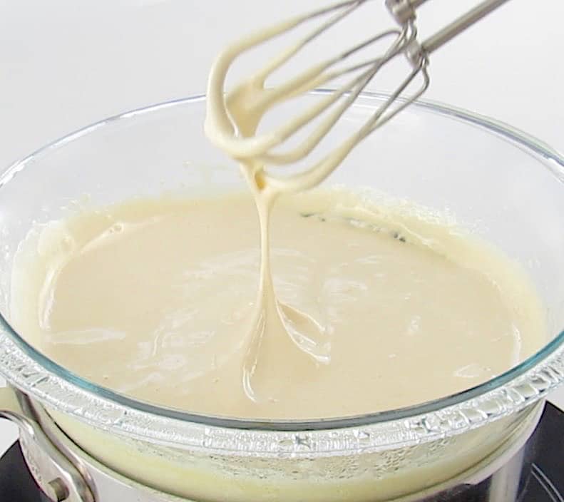custard in glass bowl over double boiler with hand mixer