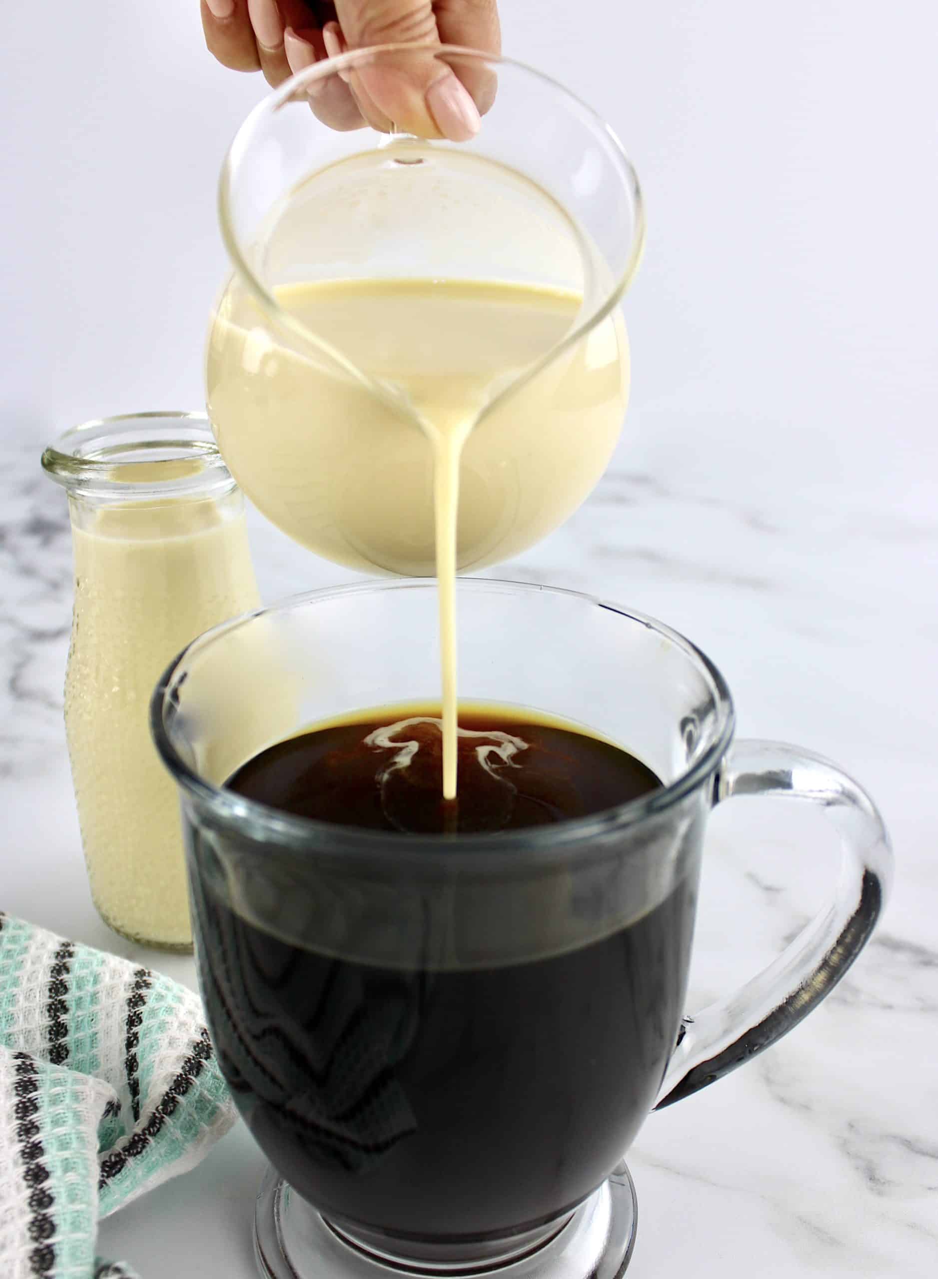 creamer being poured into black coffee in glass mug