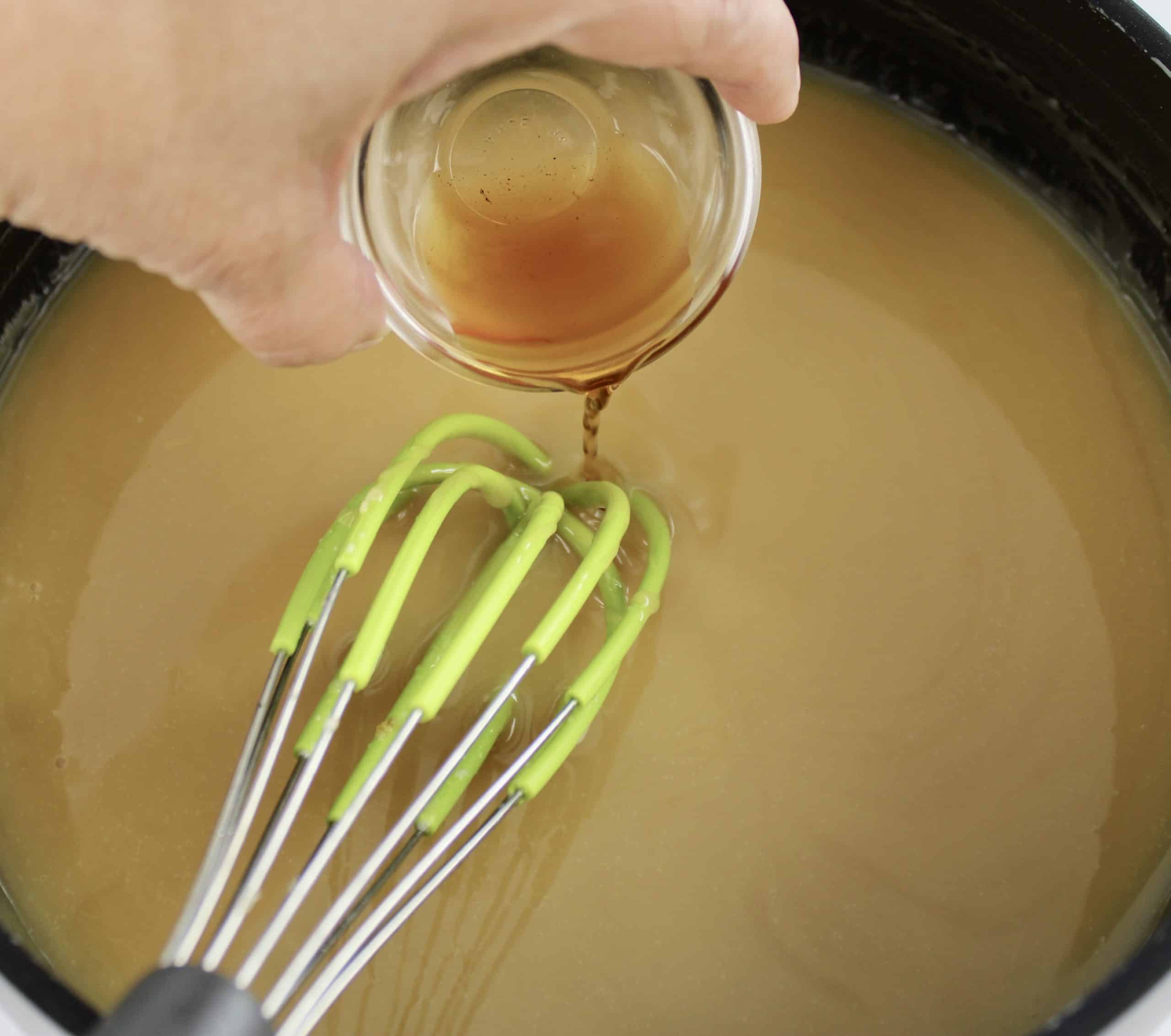 vanilla being poured into saucepan with sweetened condensed milk and whisk