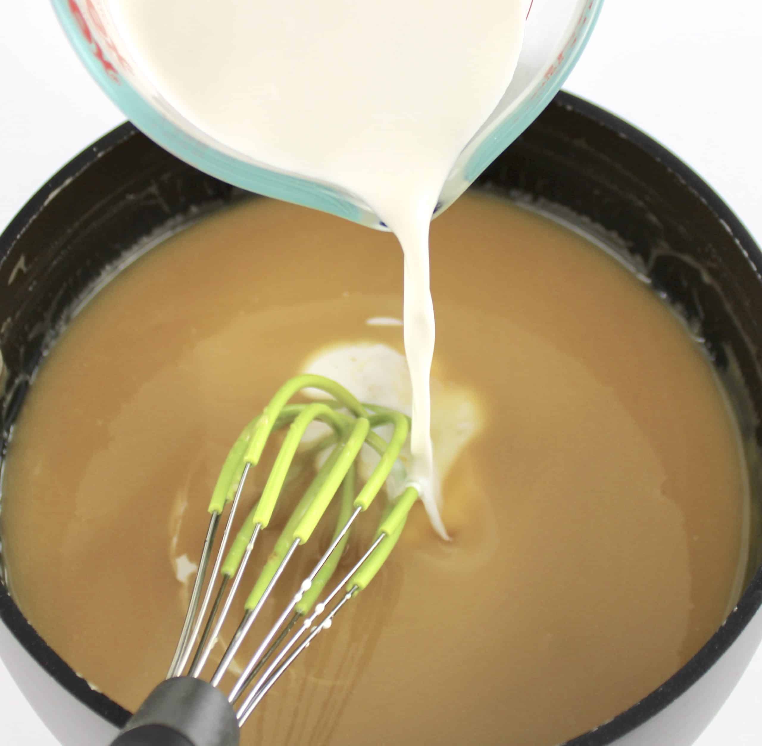 milk being poured into sweetened condensed milk in saucepan with whisk