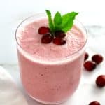 cranberry smoothie in glass with cranberries and mint leaf on top