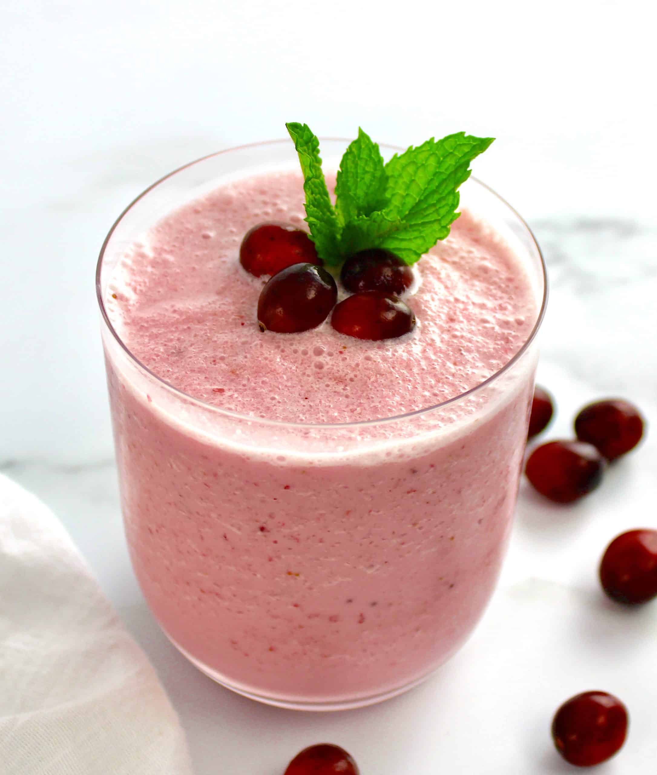 cranberry smoothie in glass with cranberries and mint leaf on top