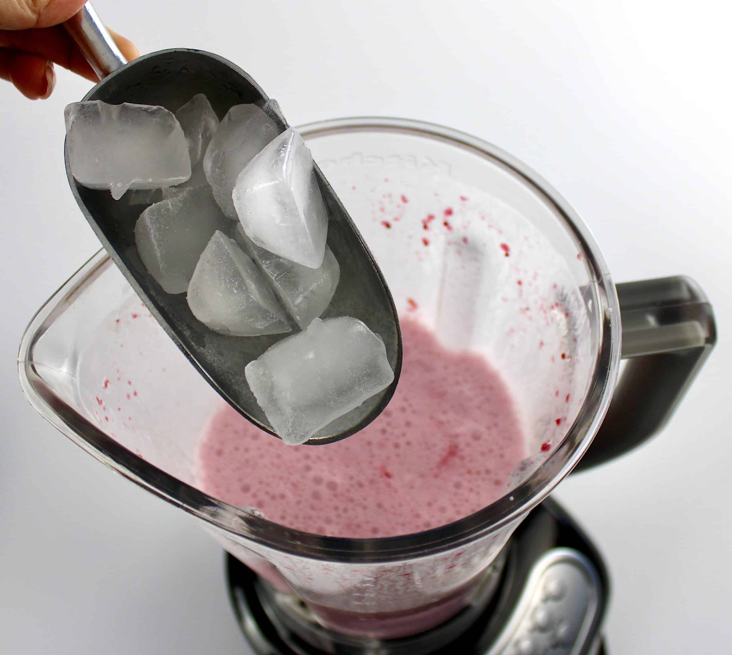 ice being scooped into blender with cranberry smoothie