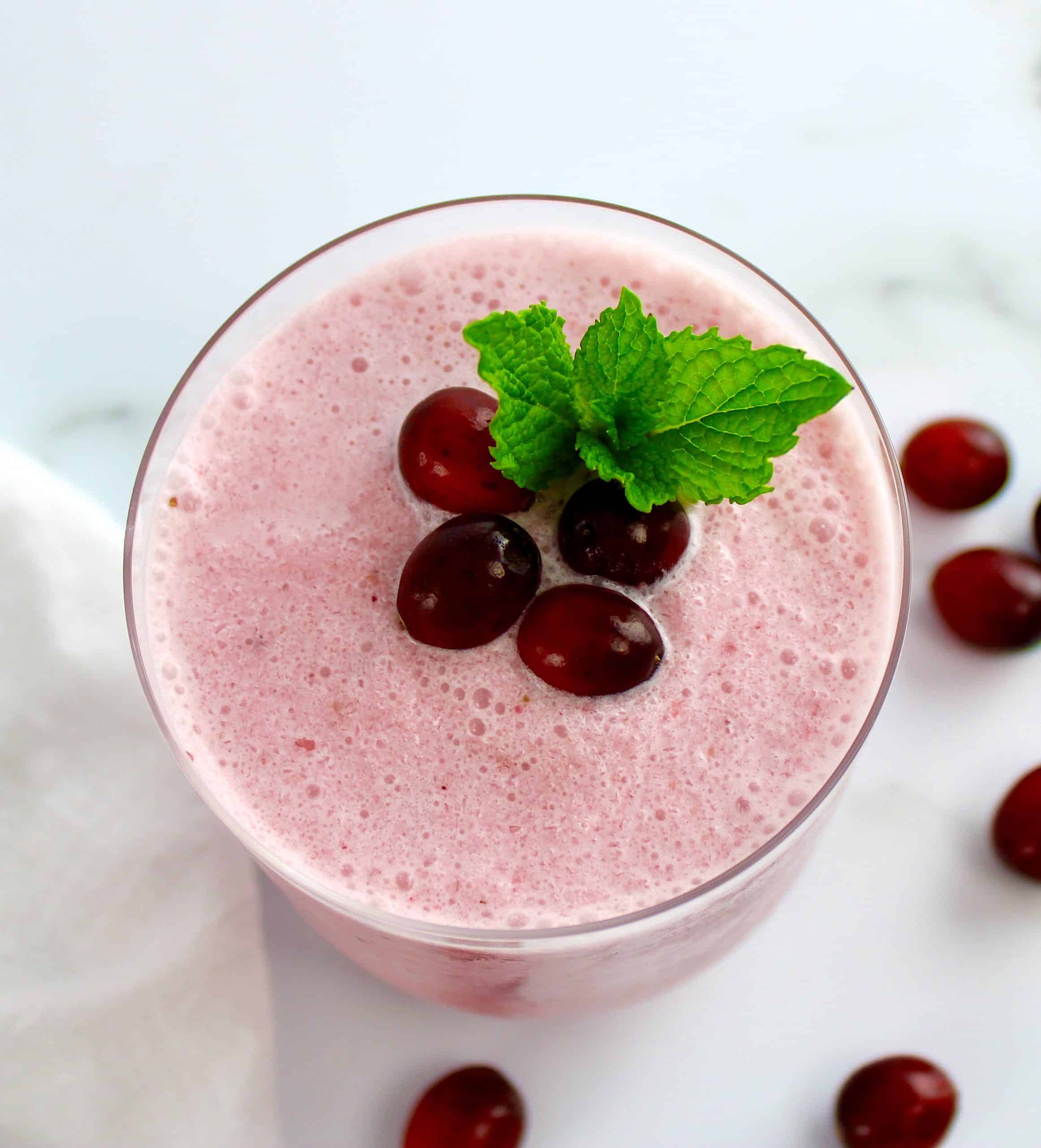 overhead view of Cranberry Smoothie in glass with cranberries and mint leaves on top