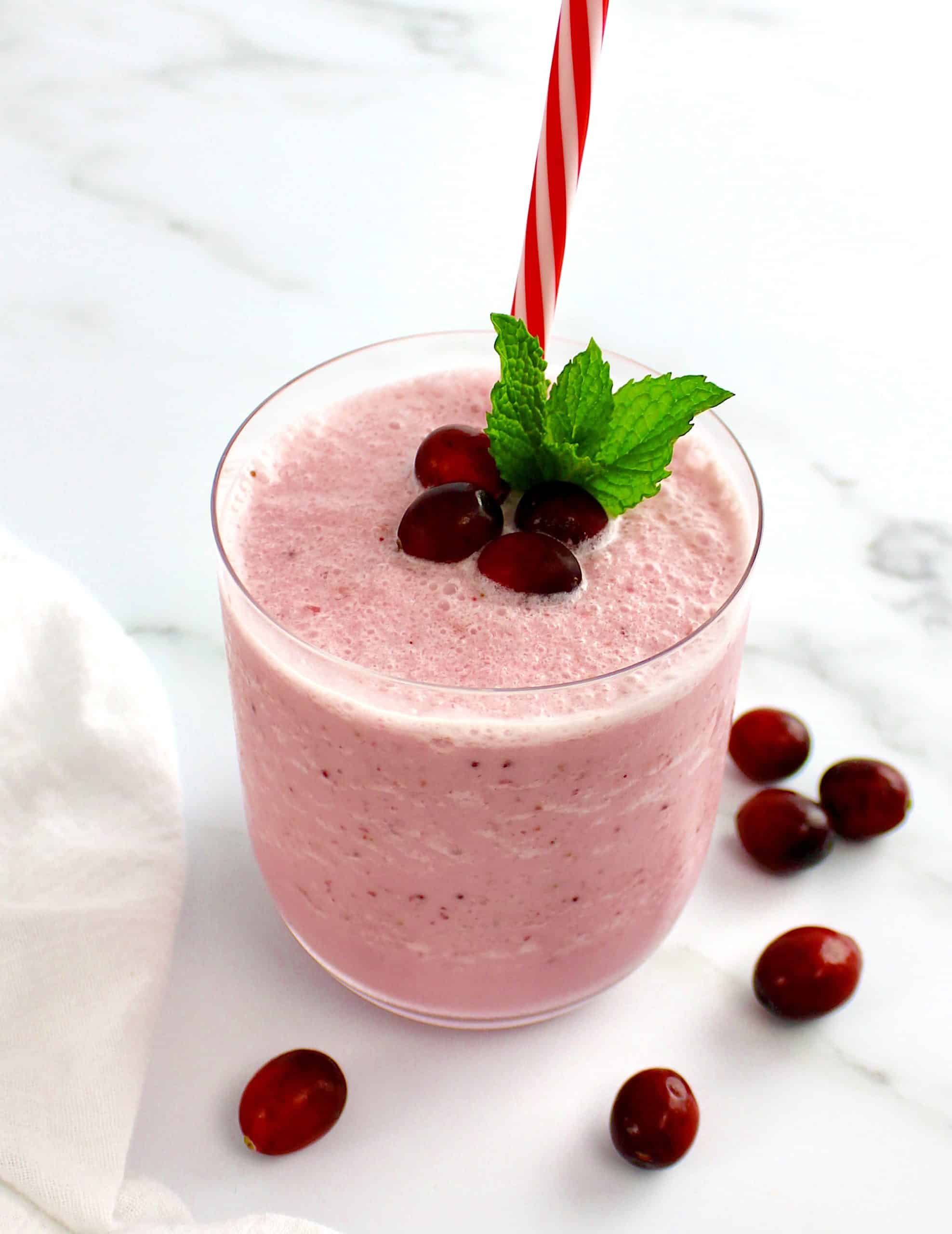 side view of cranberry smoothie with cranberries and mint leaves on top