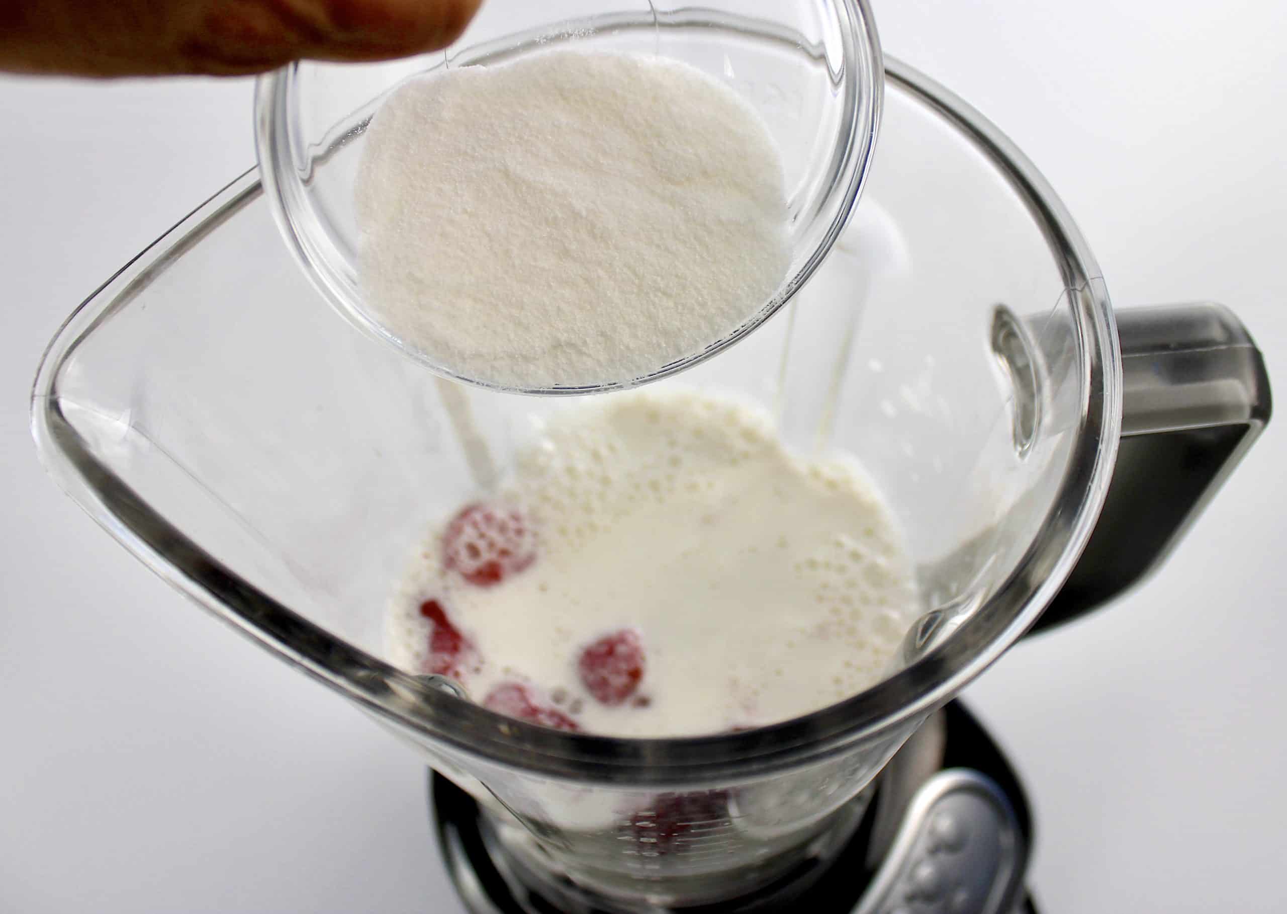 sweetener being poured into blender with milk and berries