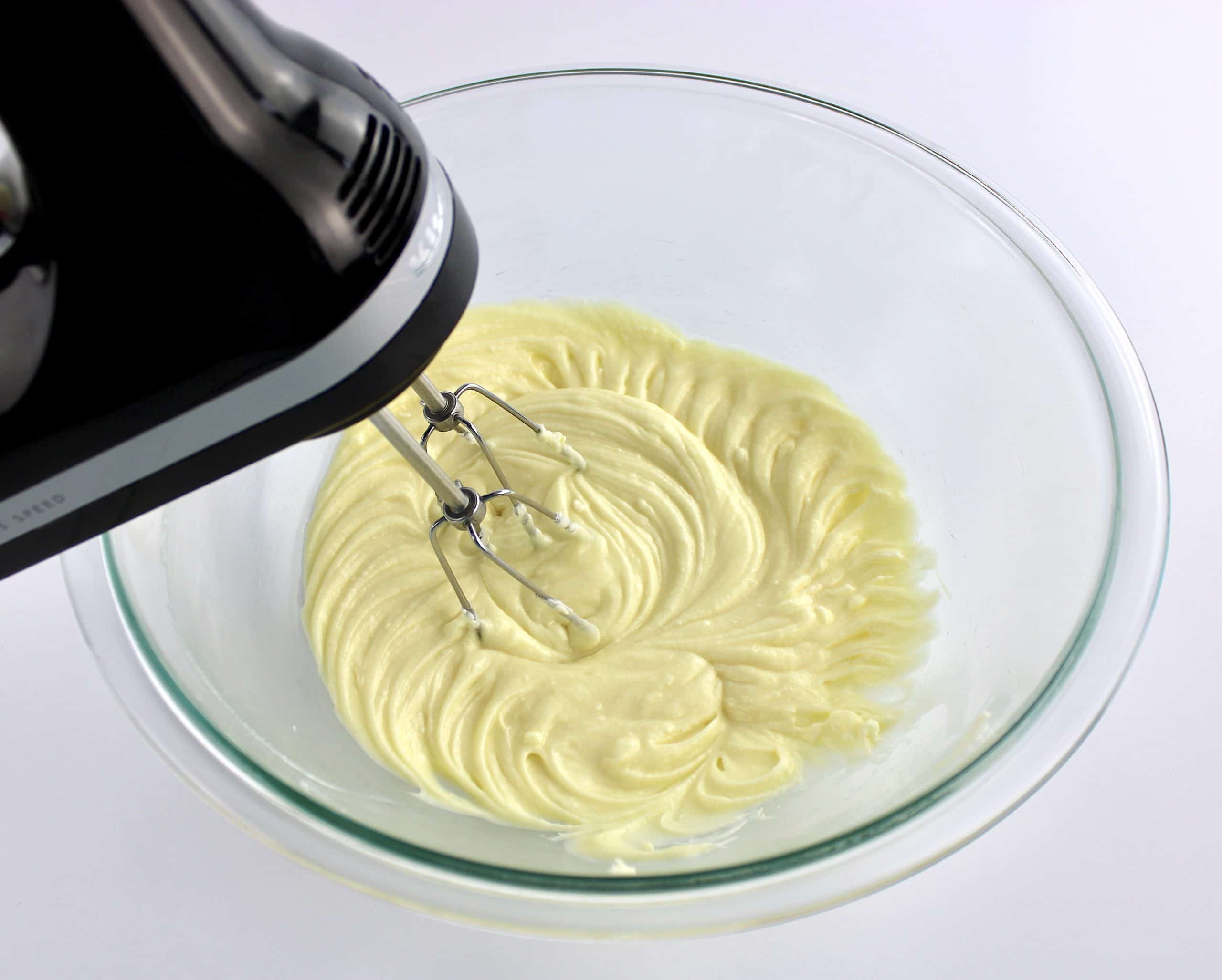 butter and sugar being creamed in glass bowl with hand mixer