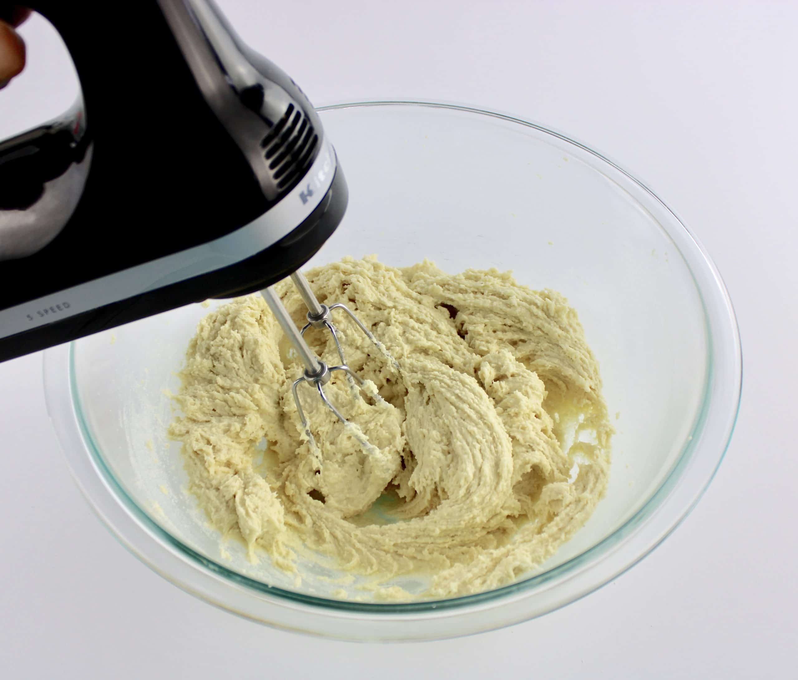 cream cheese cookie dough being mixed with hand mixer in glass bowl