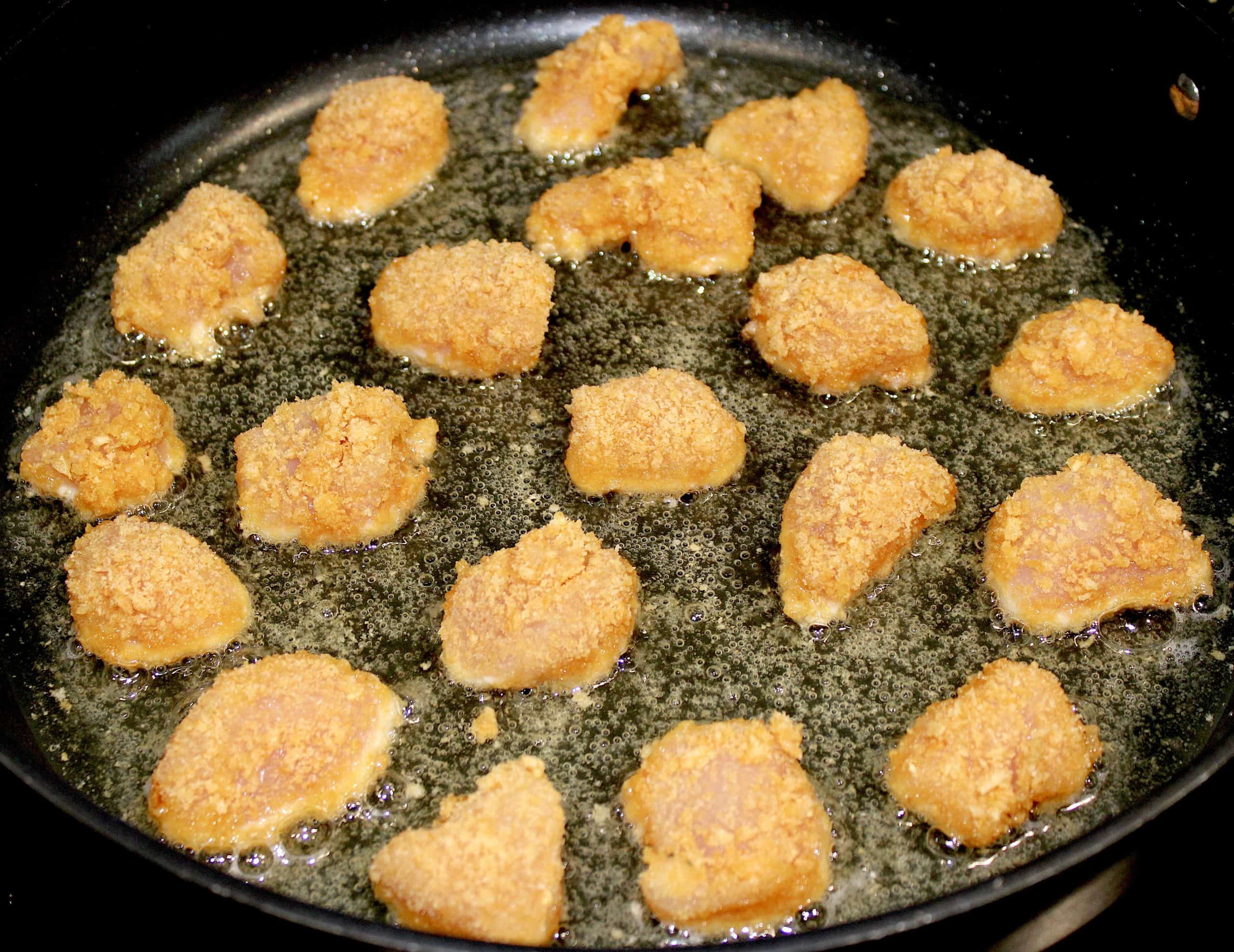 breaded chunks of chicken frying in skillet