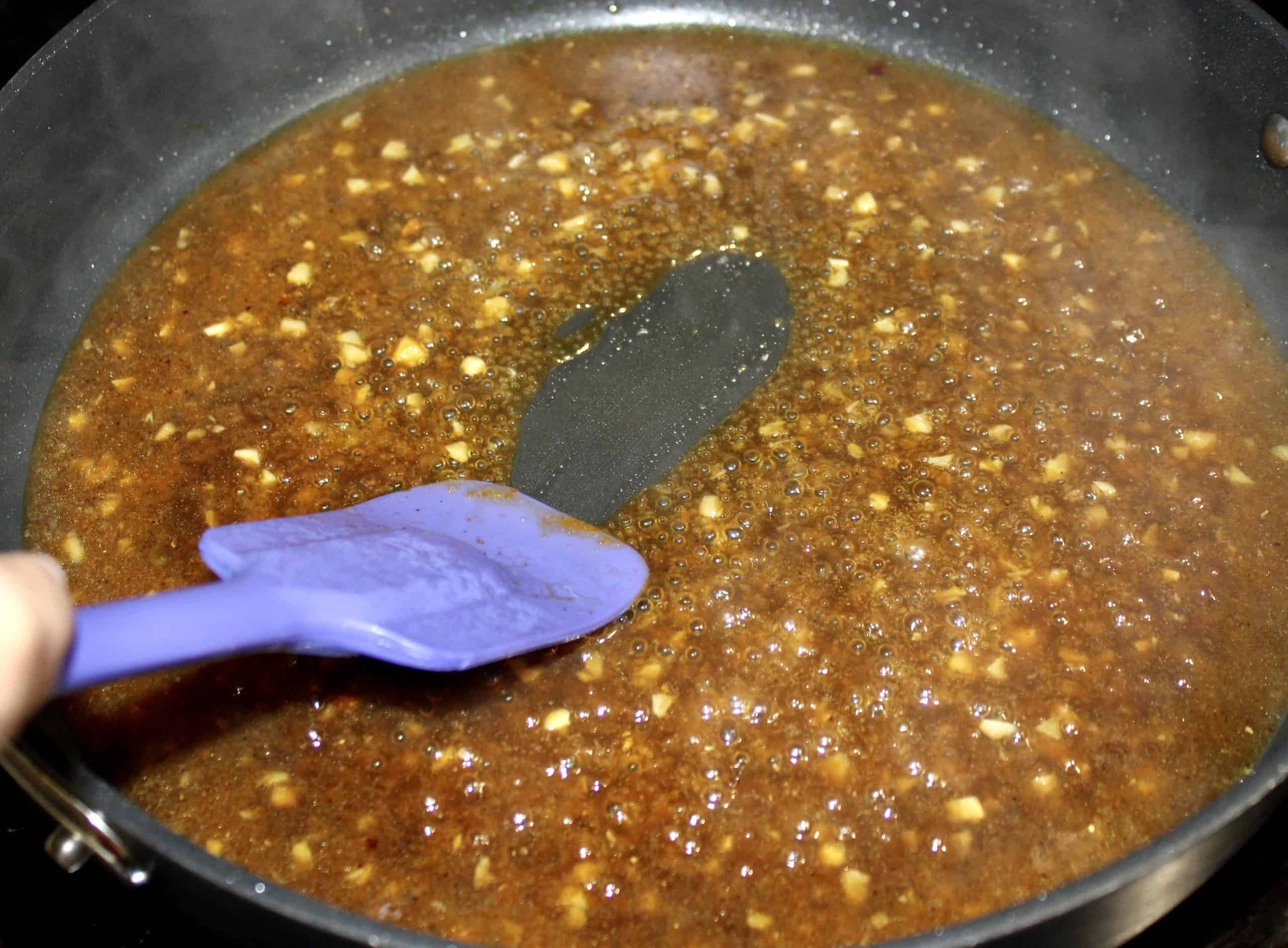 thickened orange chicken sauce in skillet with purple spatula separating the sauce