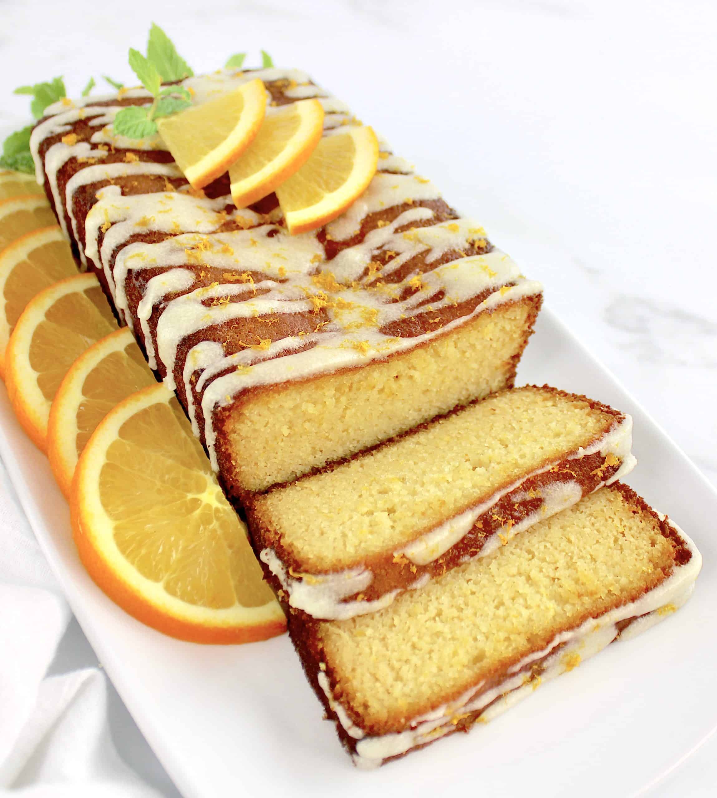 Keto Orange Pound Cake sliced on white plate with oranges 