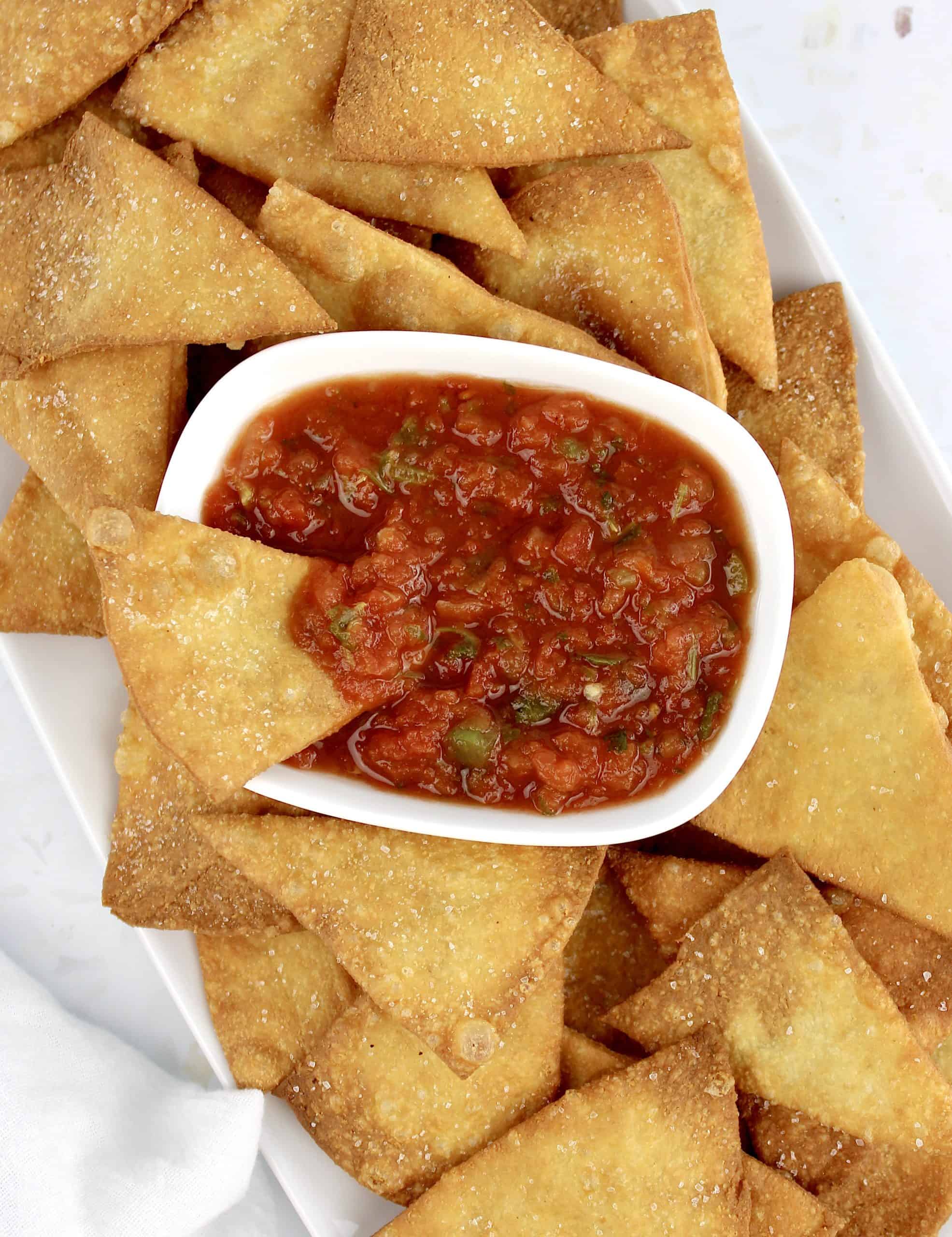 overhead view of Keto Tortilla Chips with one chip in bowl of salsa