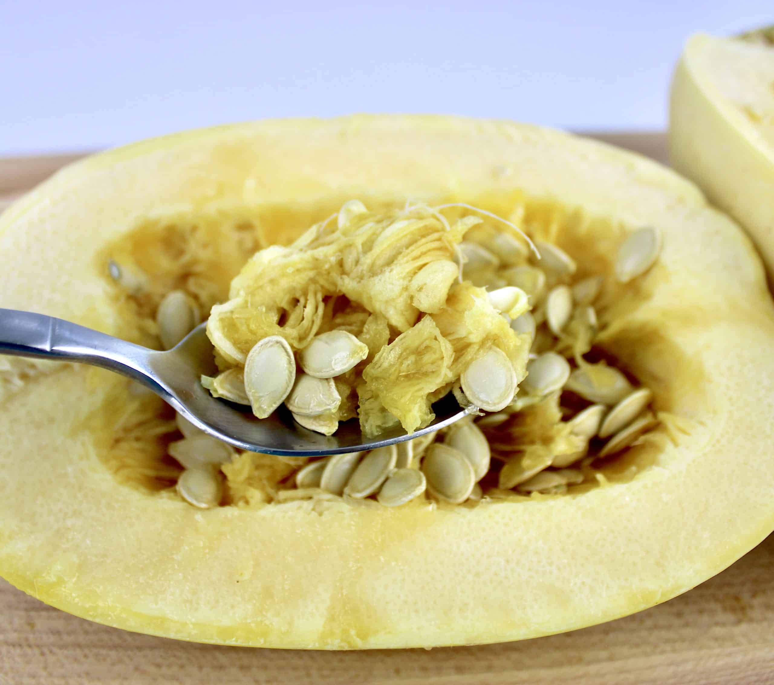 spaghetti squash cut open with seeds being spooned out