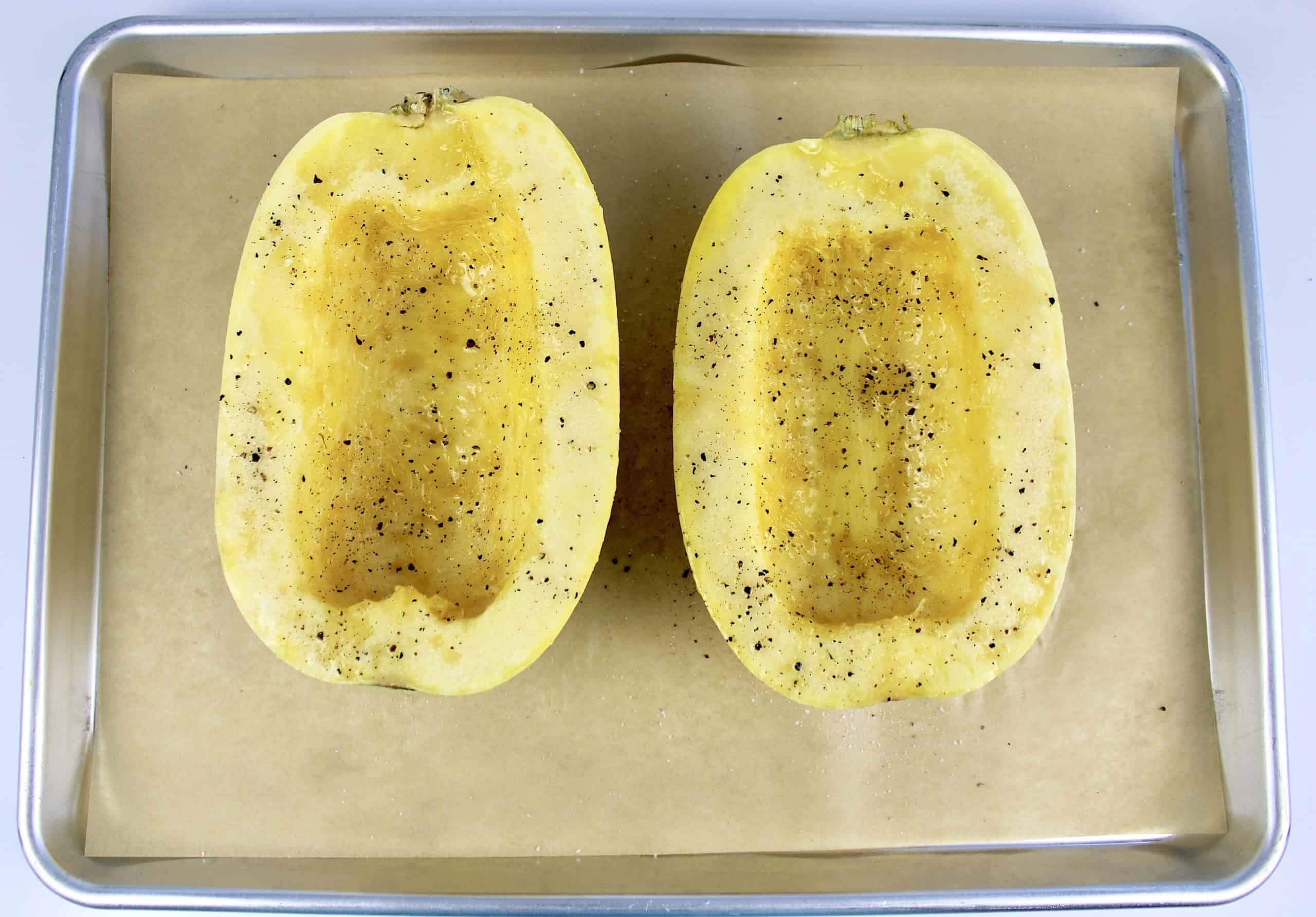 spaghetti squash cut open with olive oil salt and pepper on top of sheet pan with parchment paper