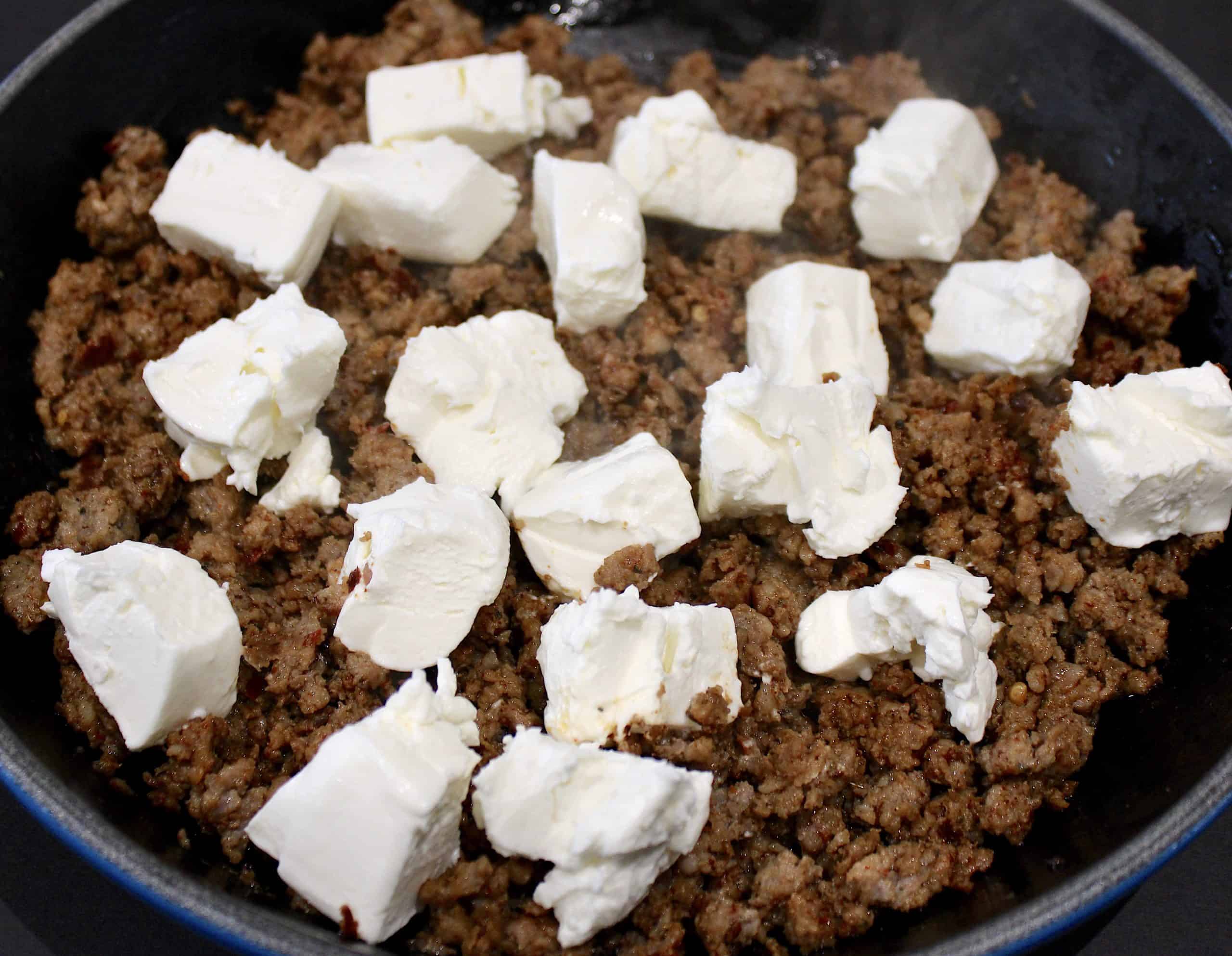 ground sausage cooked in skillet with chunks of cream cheese