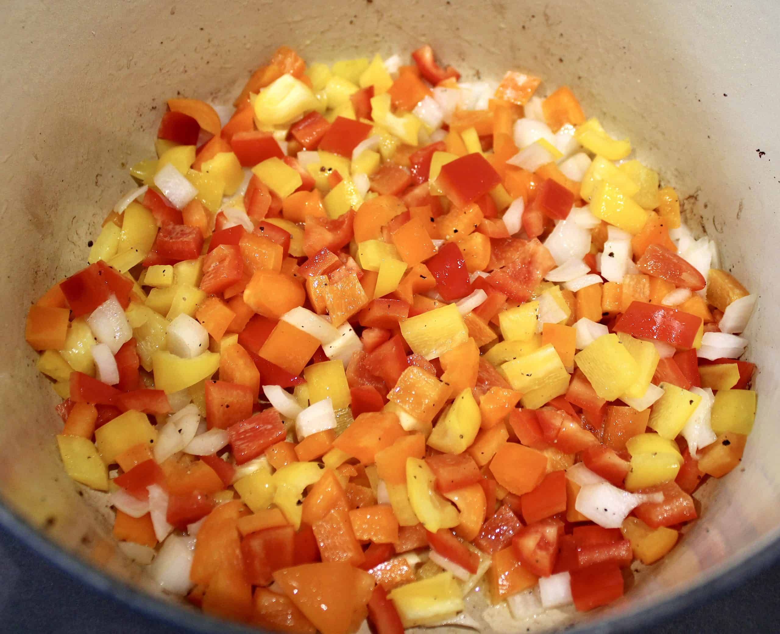 red yellow and orange peppers with onions sauteeing in pot