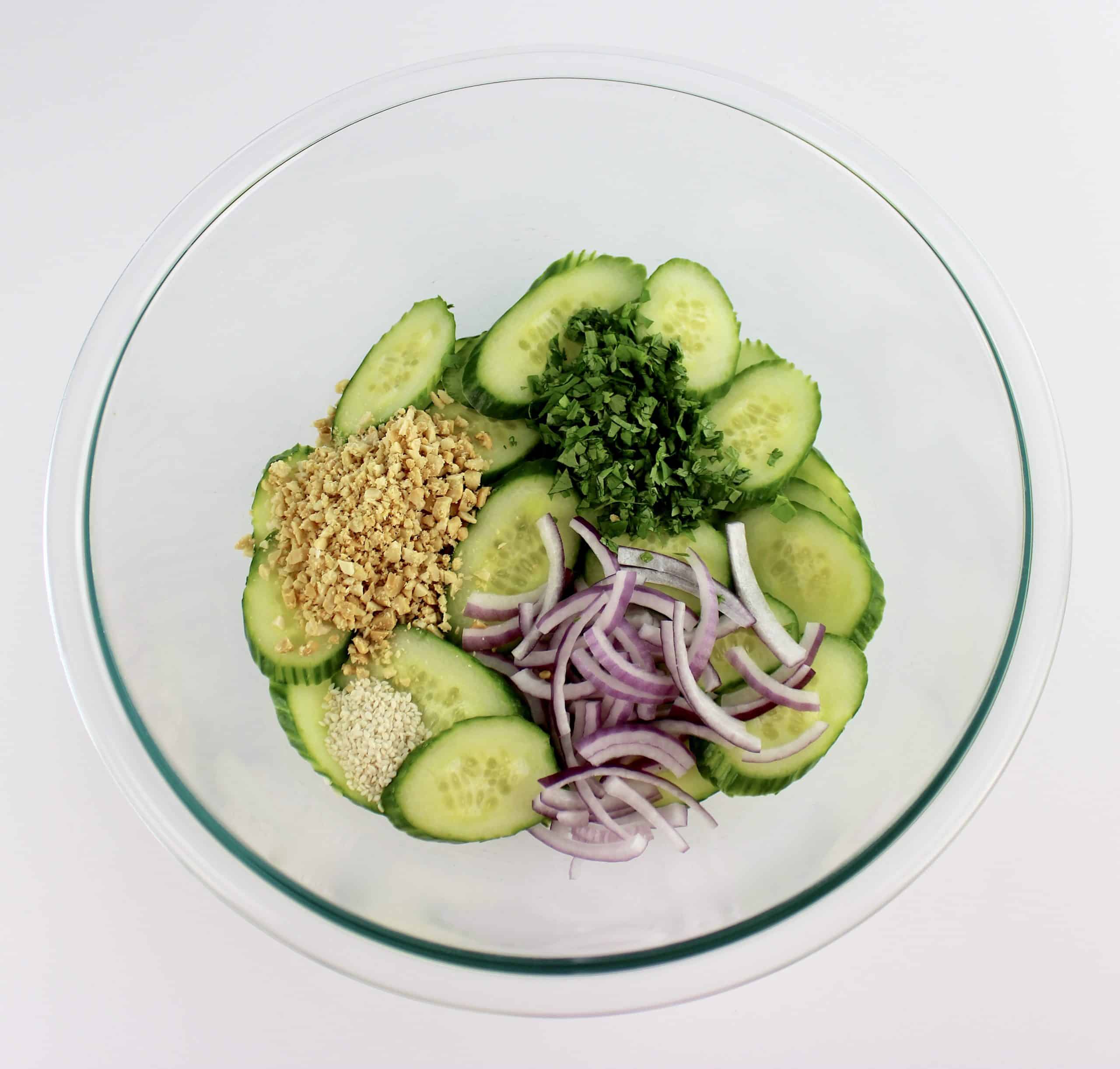 cucumber slices chopped peanuts red onion cilantro and sesame seeds in glass bowl
