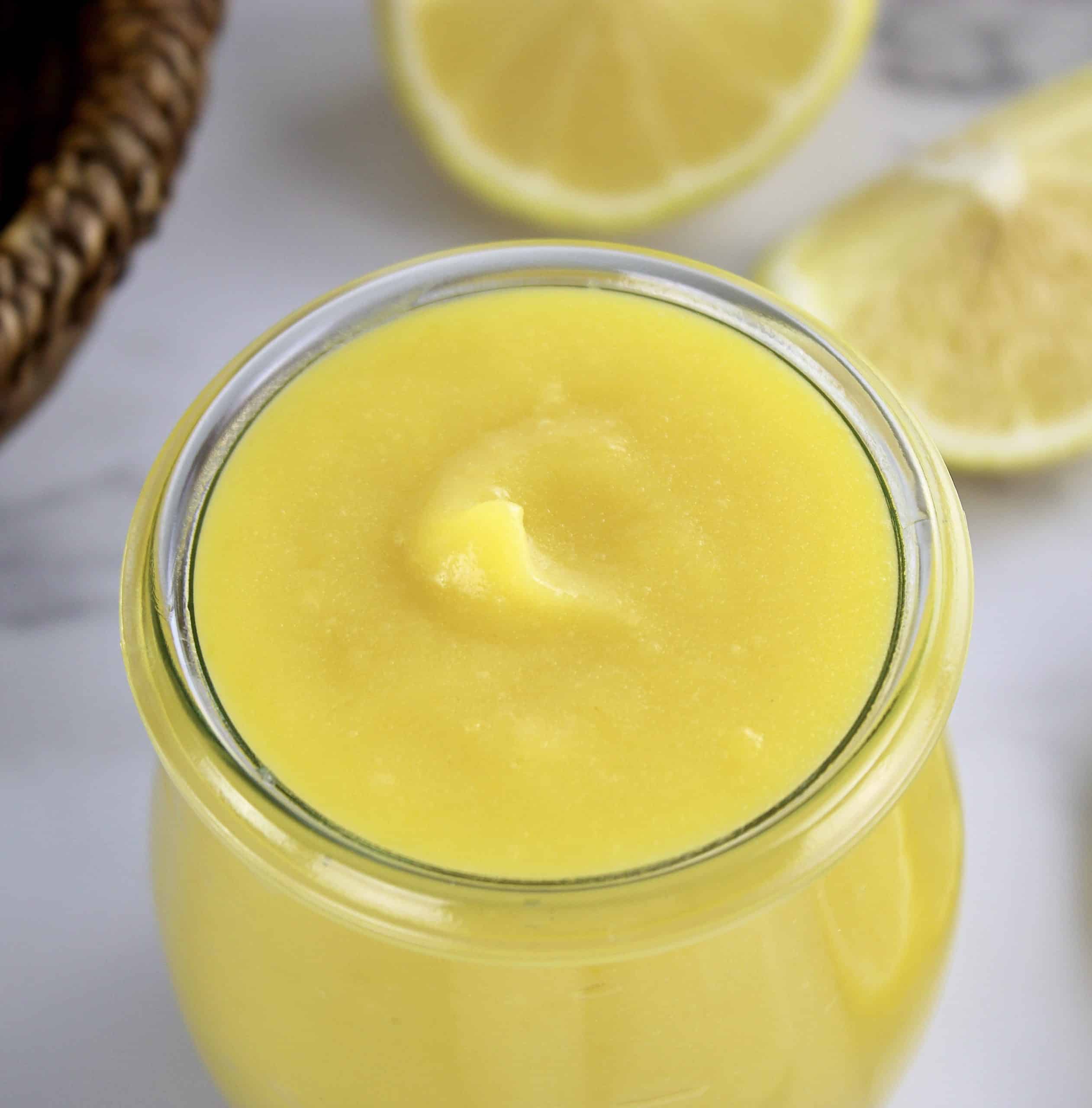 closeup of lemon curd in open jar with lemons in background