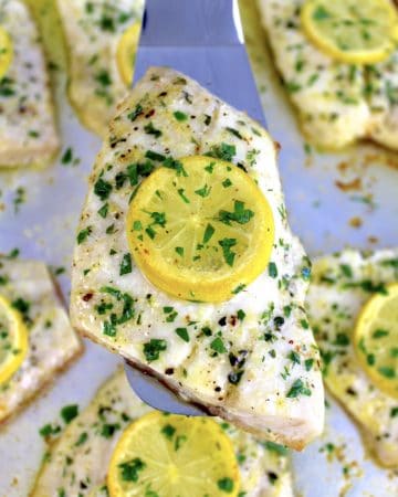piece of baked red snapper with herbs and lemon slice on top being held up with silver spatula