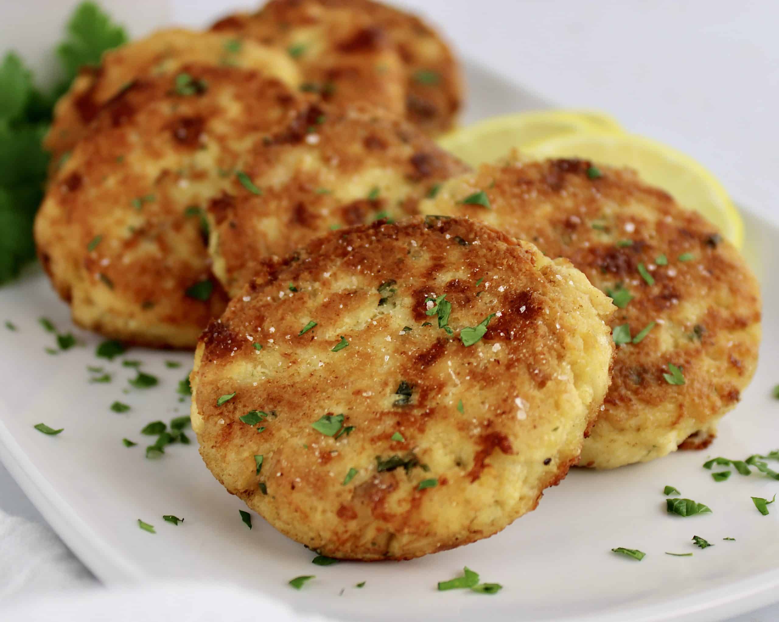 closeup of chicken patties on white plate with parsley garnish