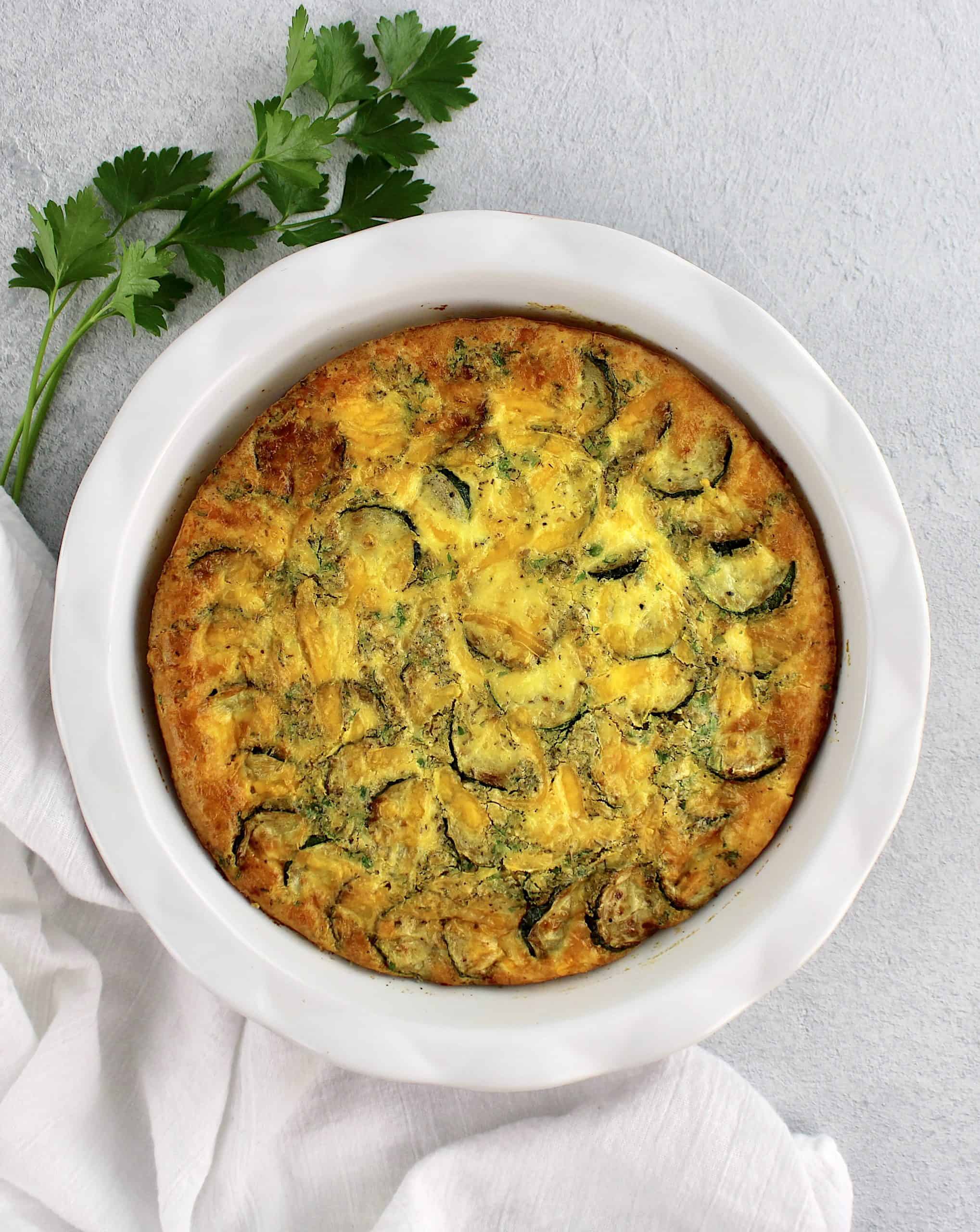 Crustless Zucchini Quiche in white pie dish with parsley on side
