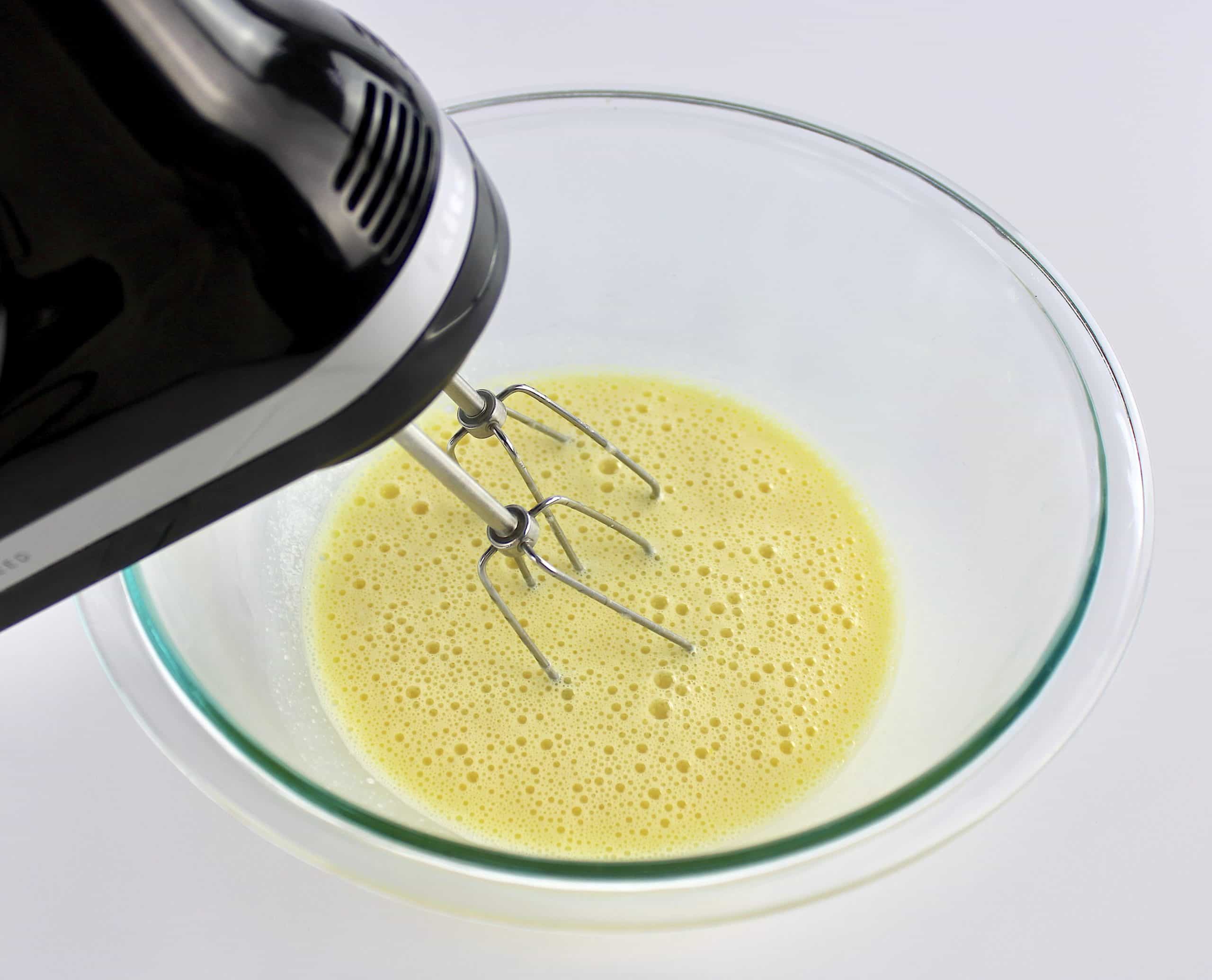 wet ingredients being whipped with hand mixer in glass bowl