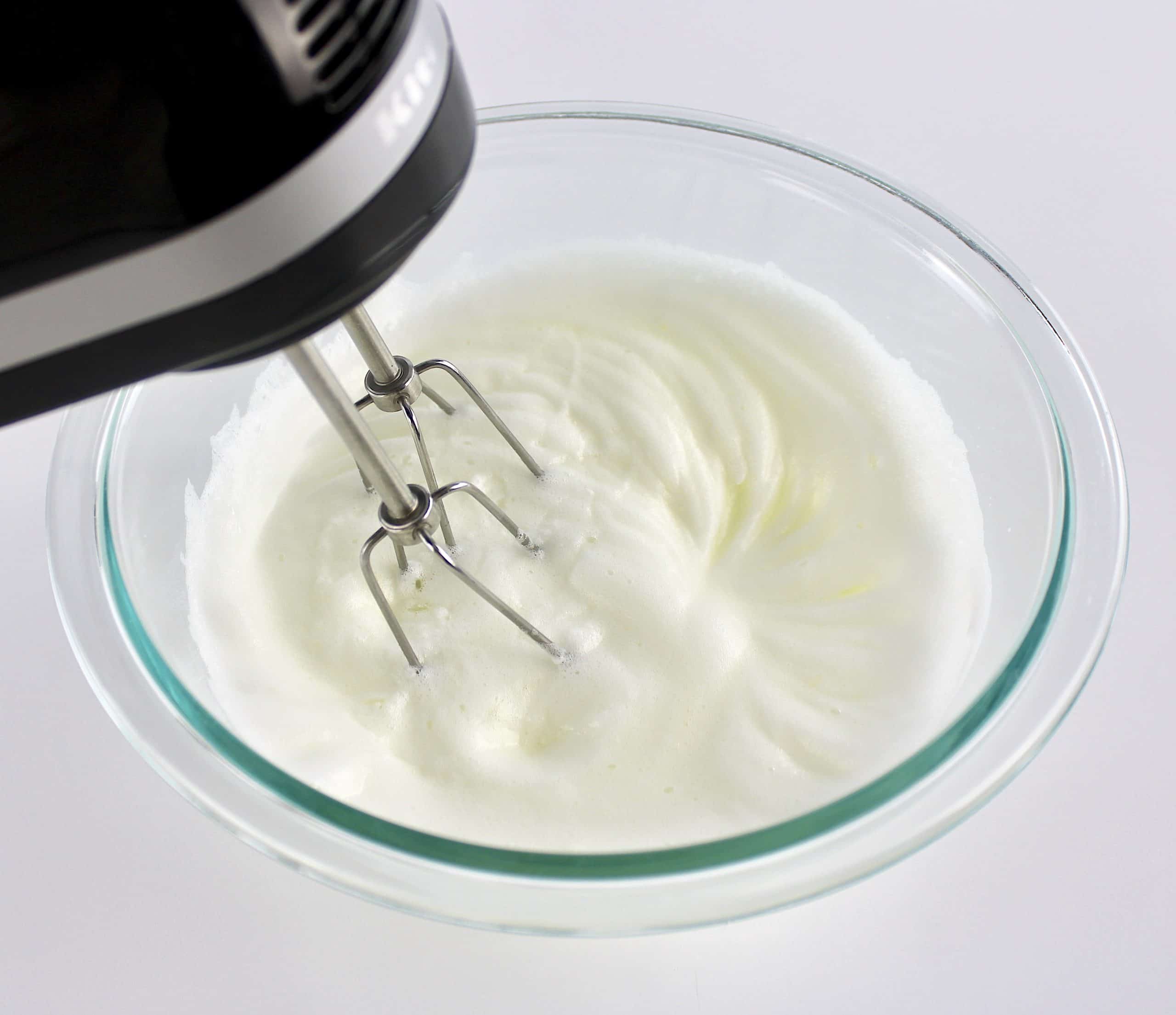 egg whites being whipped with hand mixer in glass bowl