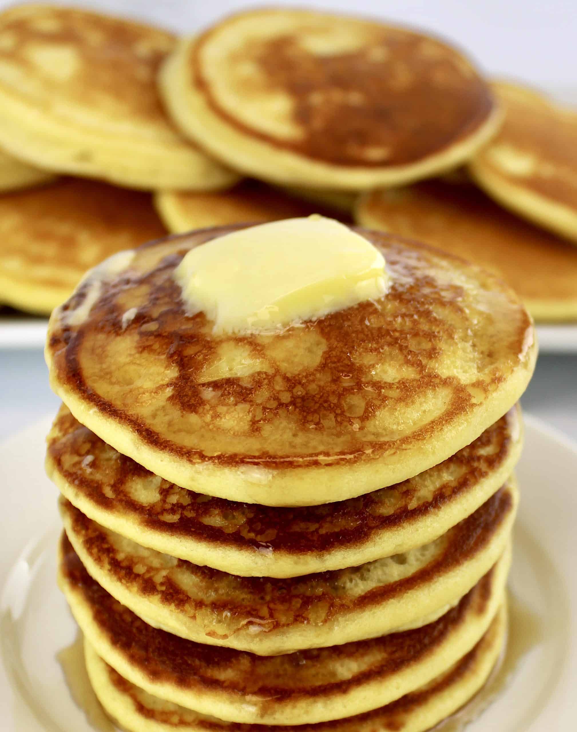 stack of pancakes with butter on top and more pancakes in background