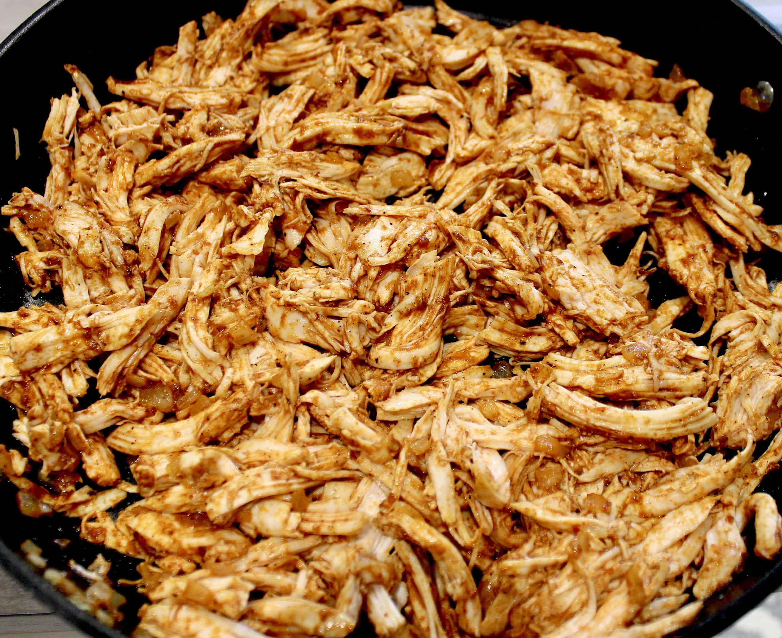 shredded chicken in skillet with enchilada sauce mixed in
