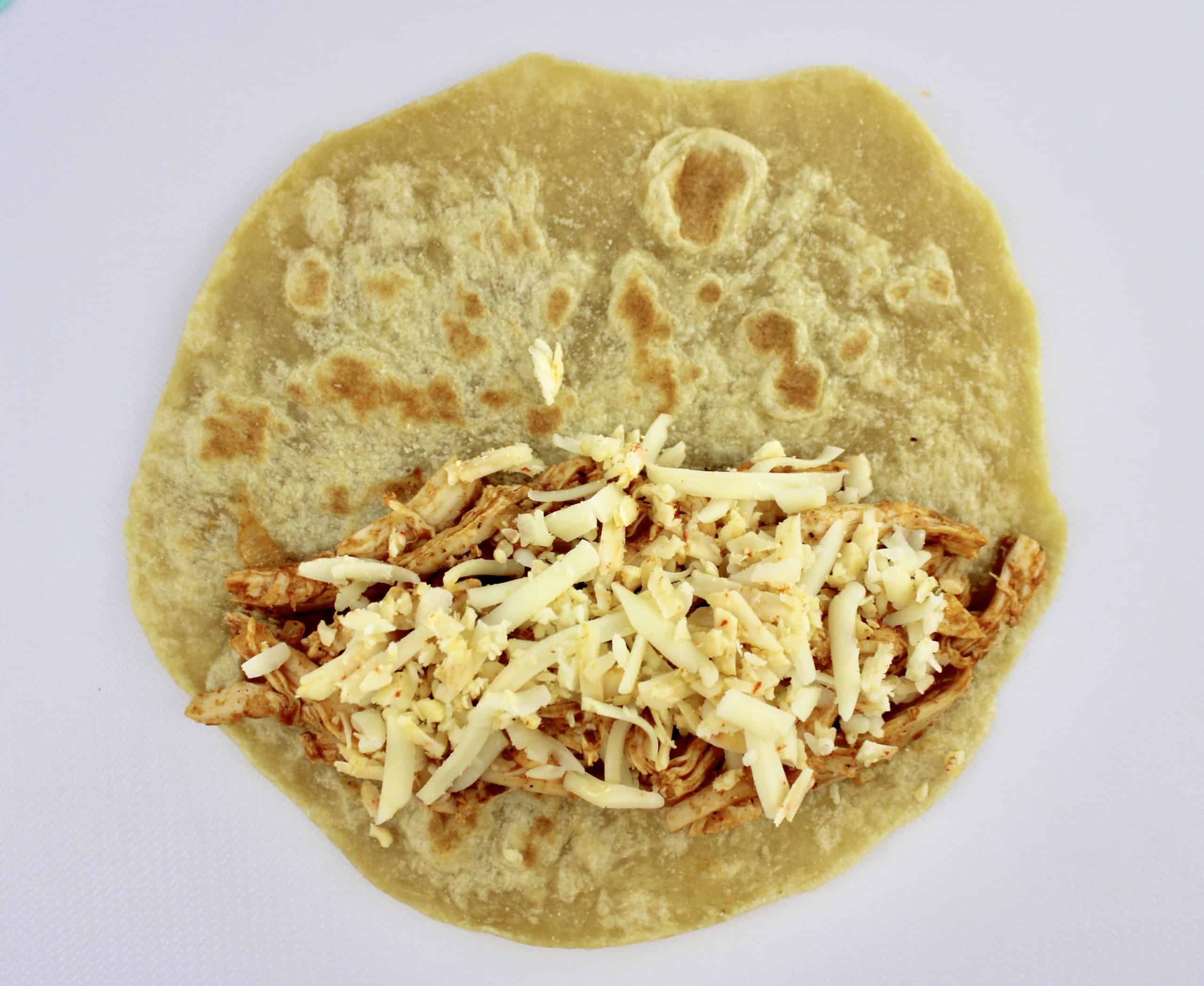 shredded chicken and cheese on open tortilla