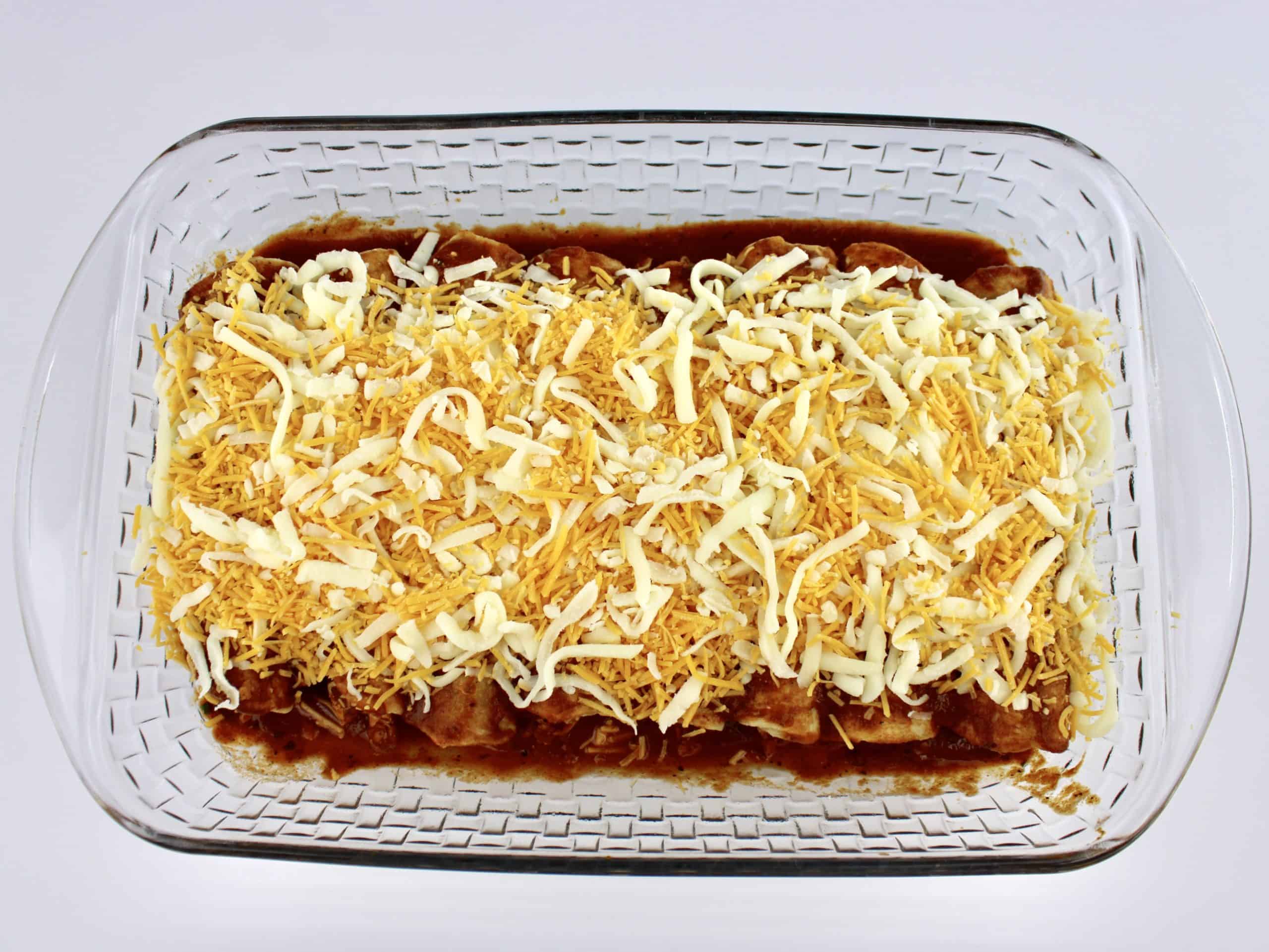 8 Chicken Enchiladas with cheese on top in glass baking dish unbaked